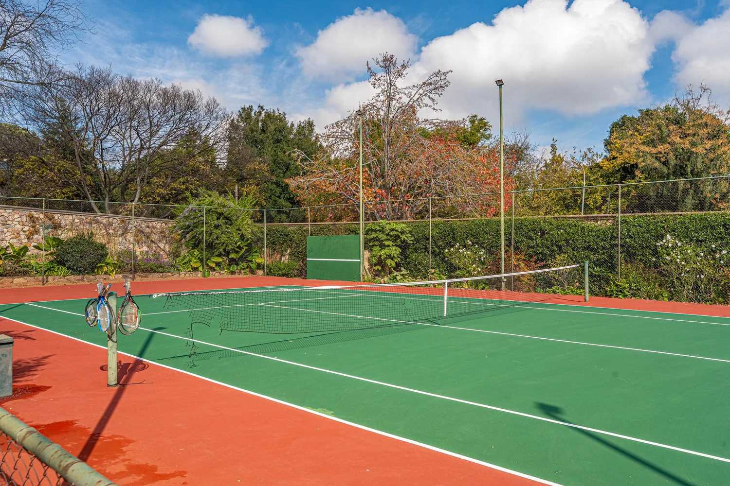 Floodlit tennis court surrounded by established trees