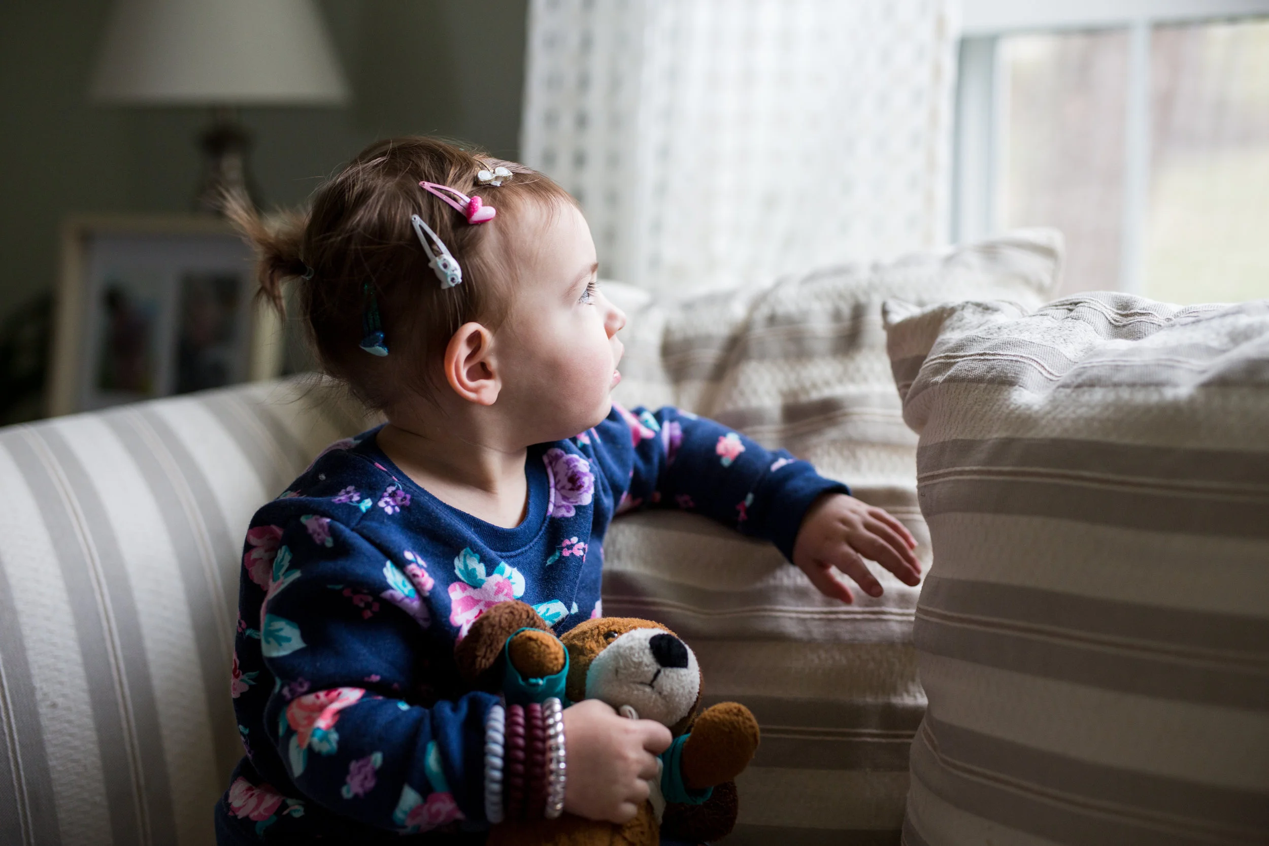 Young child looks out the window of her home, while light shines on her face