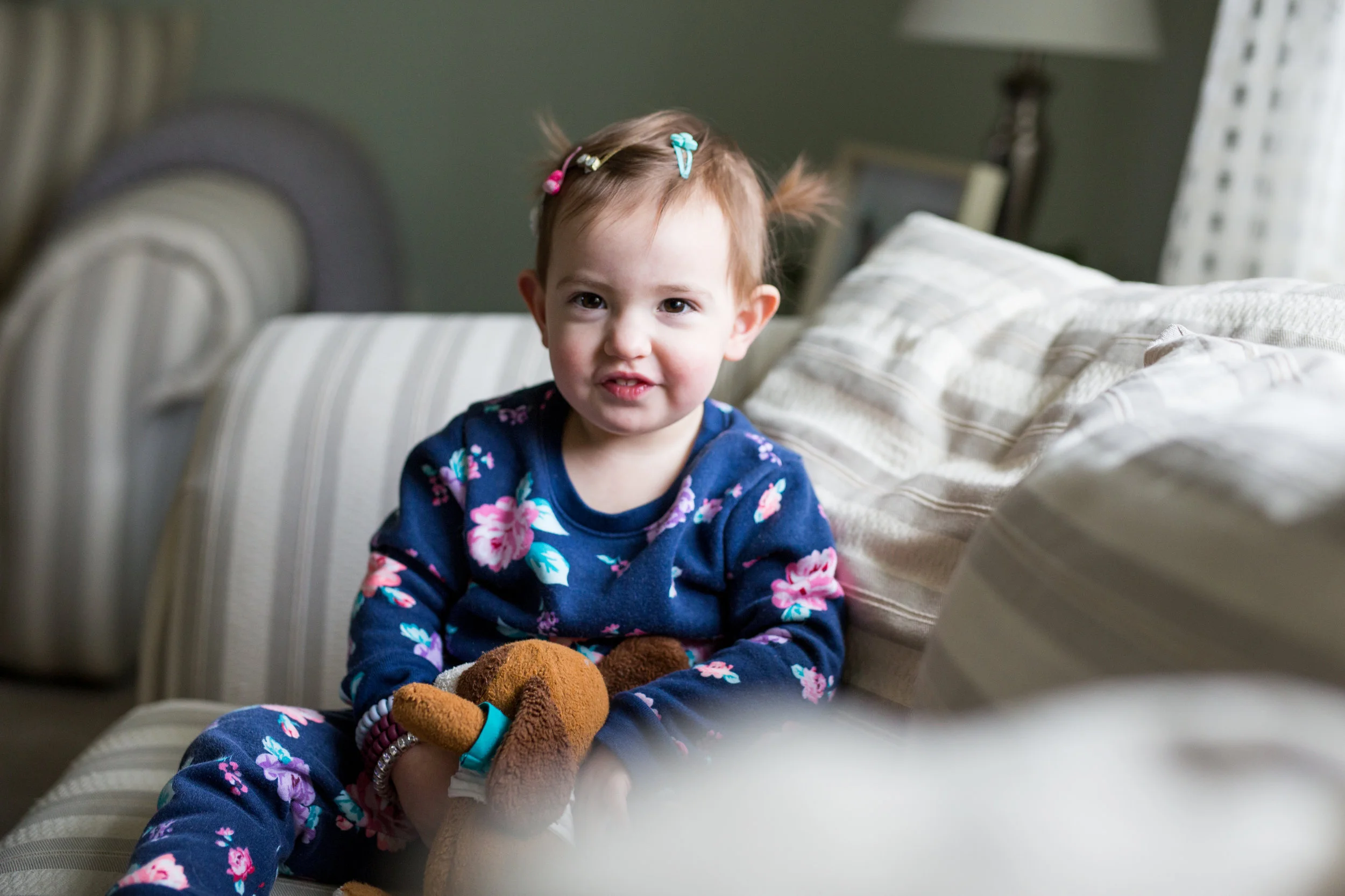 Toddler girl smiles as she sits on the couch in her Pittsburgh home
