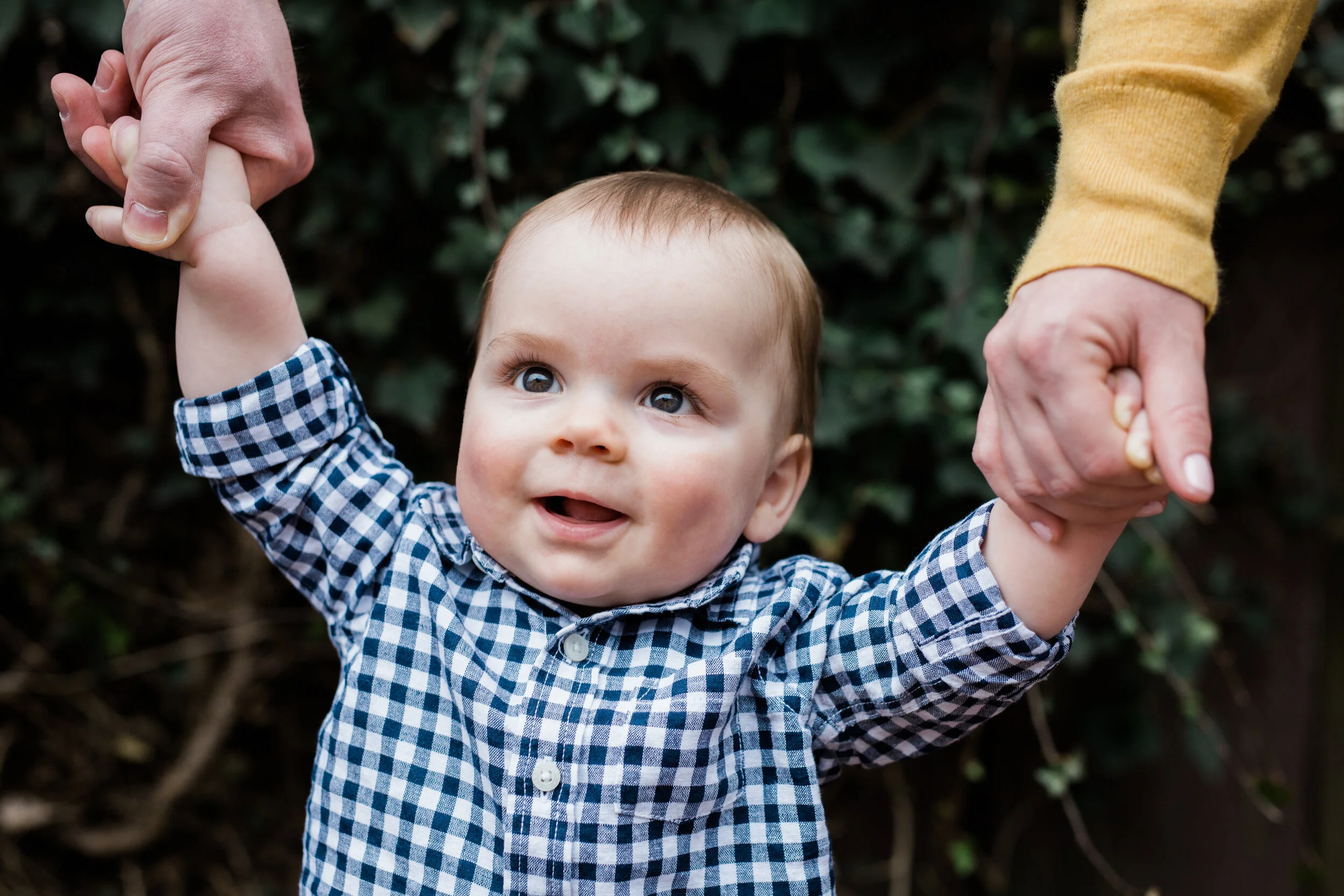 Toddler holds his parents hands outside in a Pittsburgh park