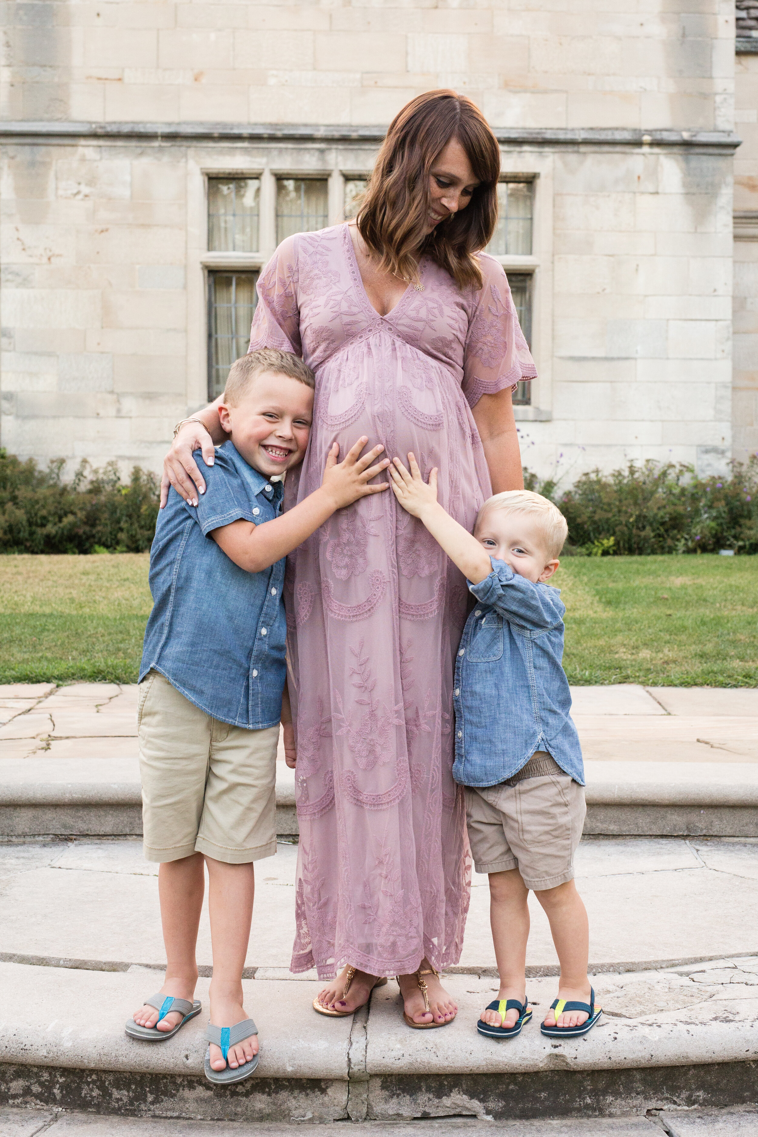 A pregnant mom looks down at her 2 sons, both touching her belly