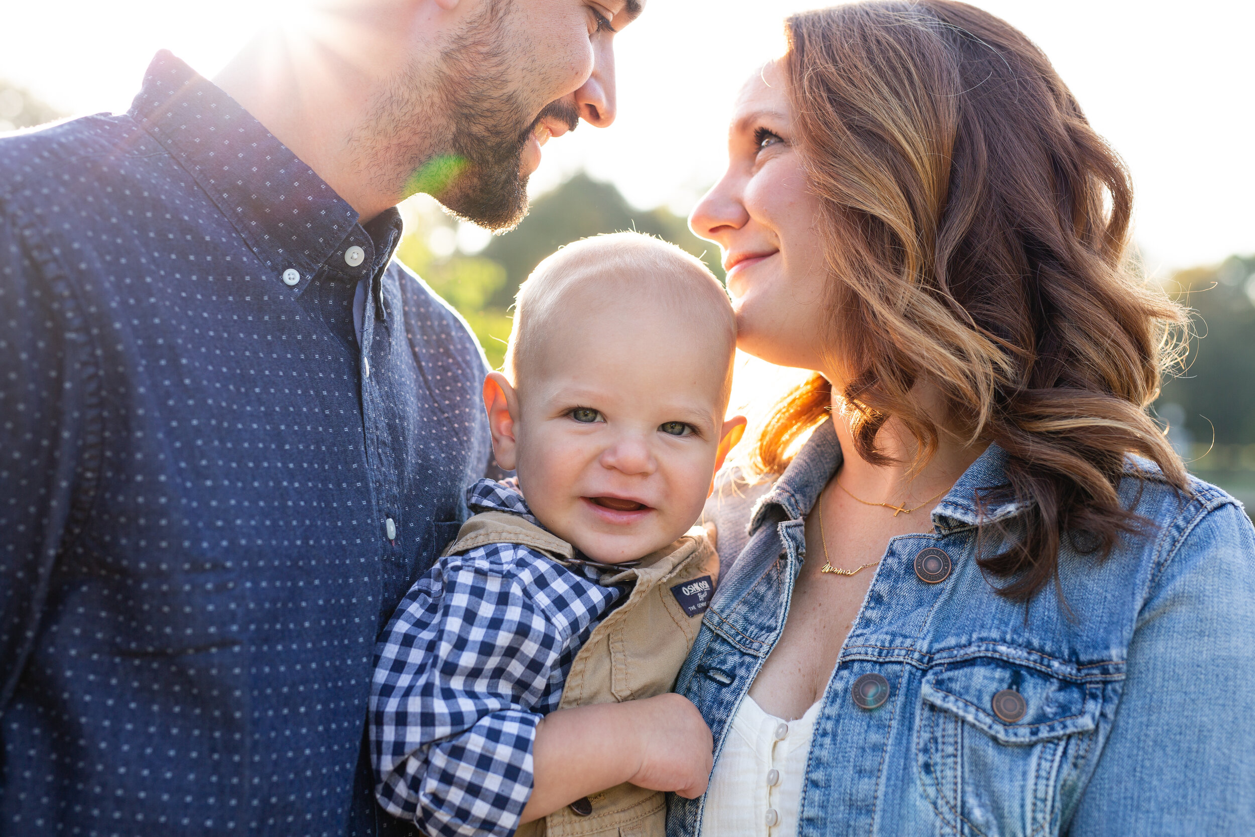 A mom and dad look at each other while they hold their child close. A sunbeam shines in.