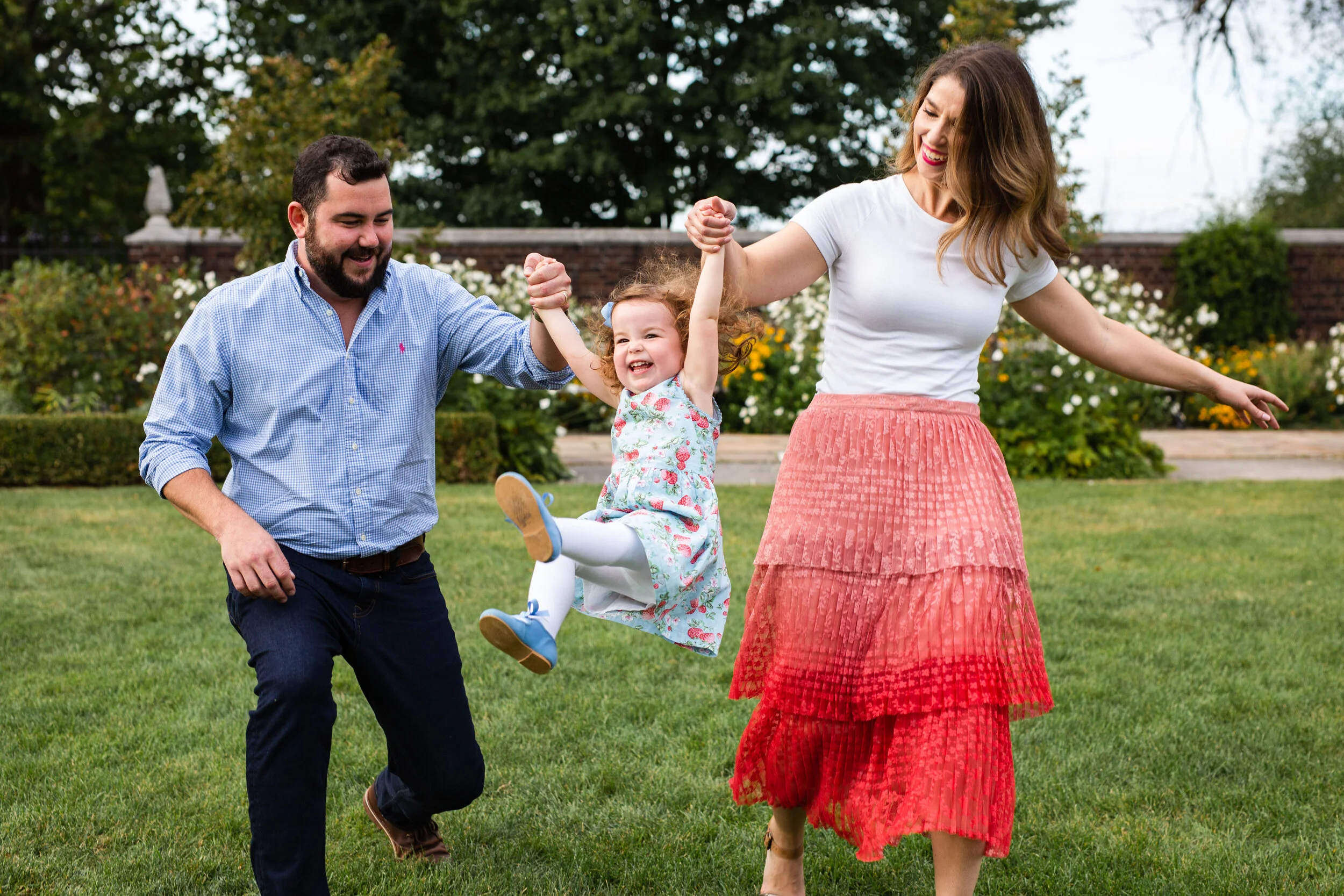 Parents swing their young child in the air. The child laughs and smiles.