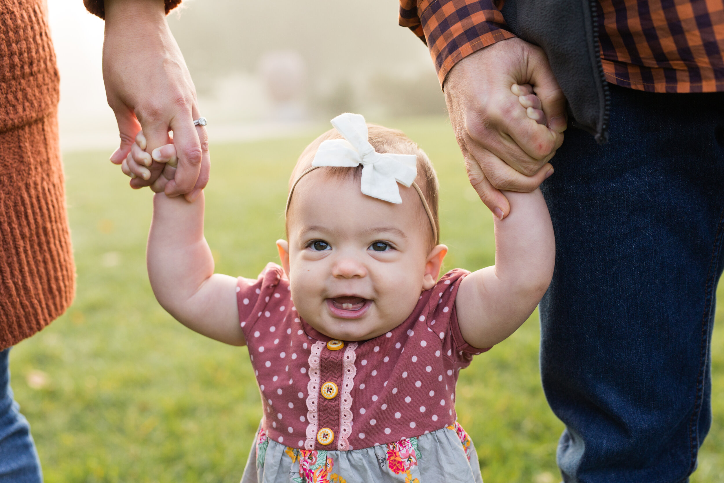 Mom and dad hold their toddler girl’s hands as she tries to walk through a Pittsburgh park