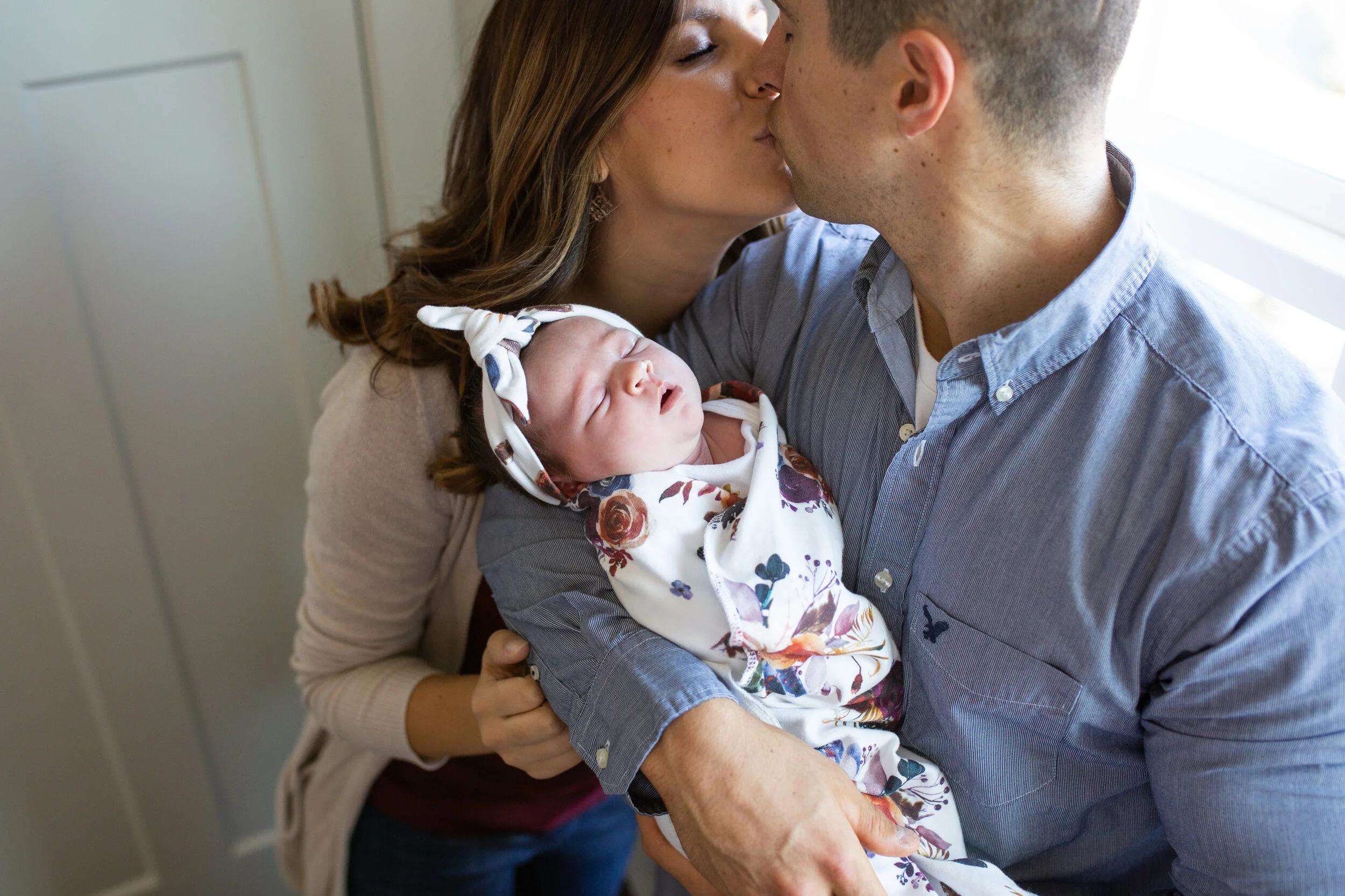 Parents kiss as the dad holds their newborn baby daughter