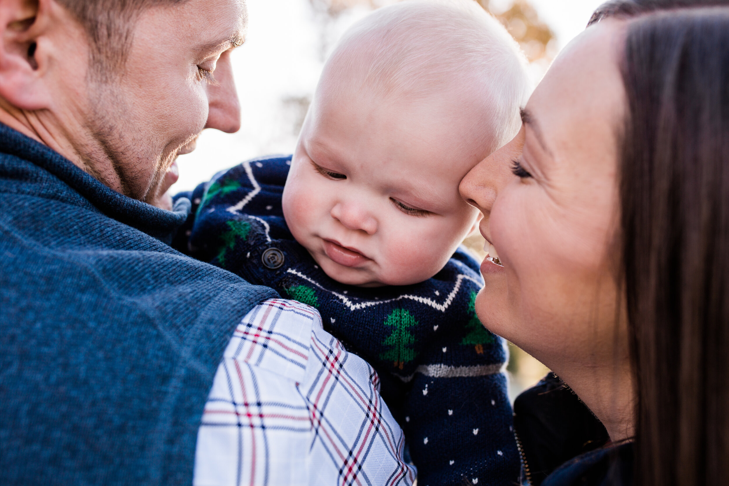 A mom and dad cuddle their baby close, smiling