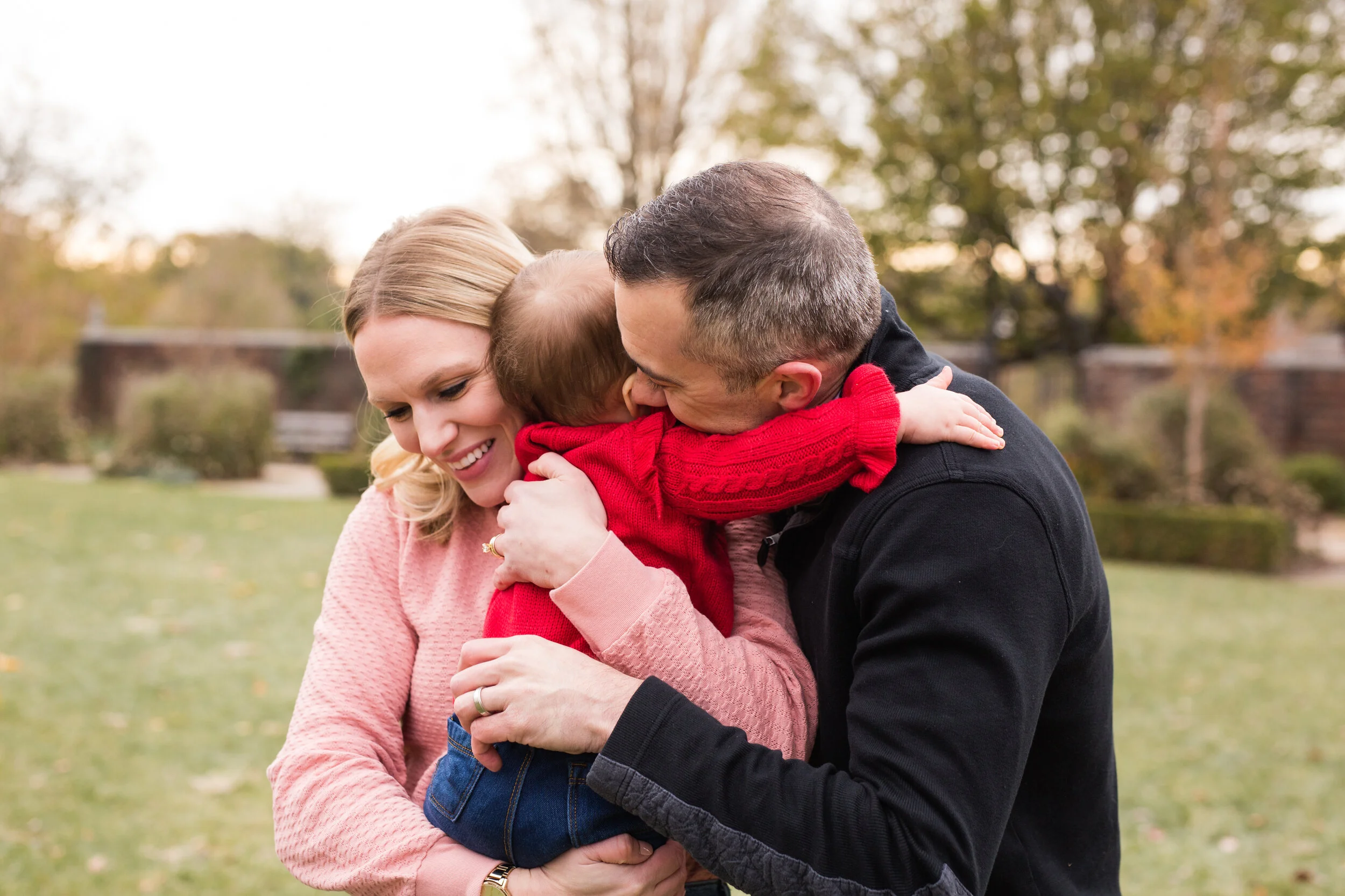 A baby girl hugs her parents, outside in a Pittsburgh park.