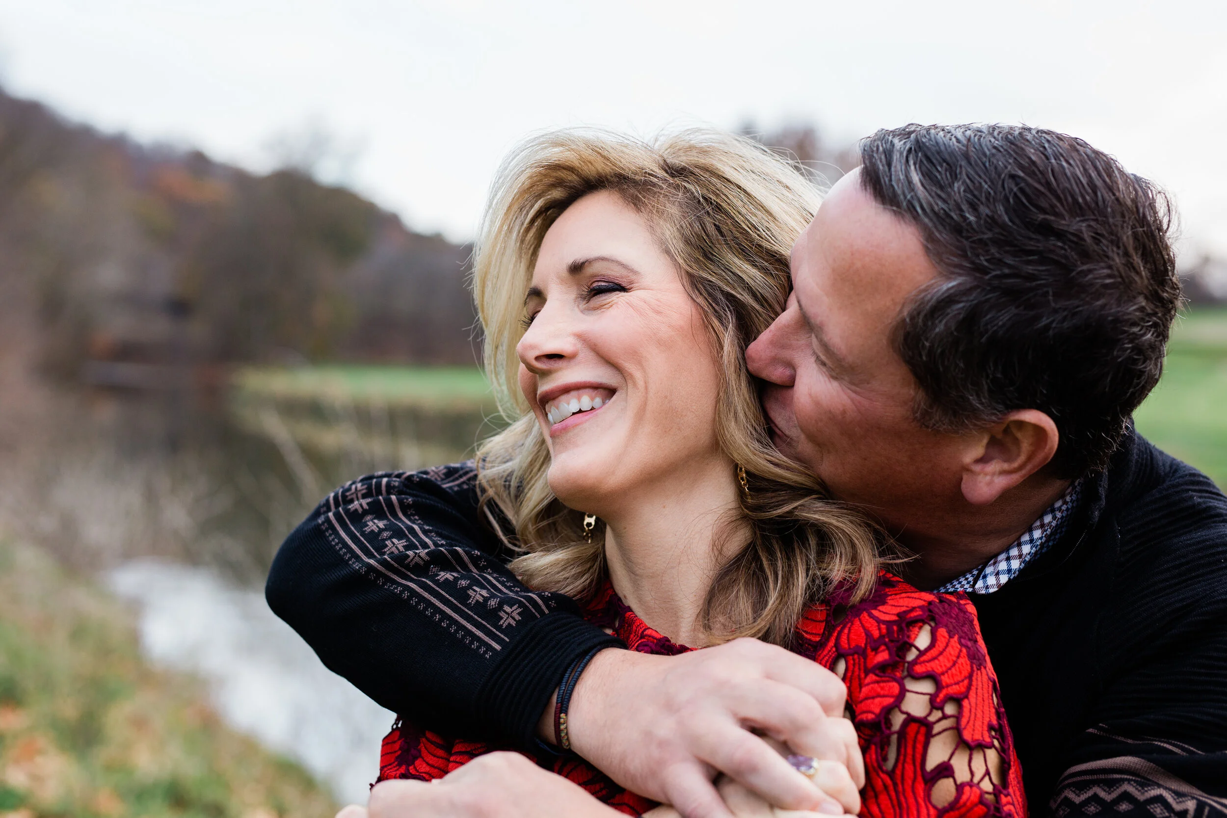 A husband kisses his wife as she smiles big