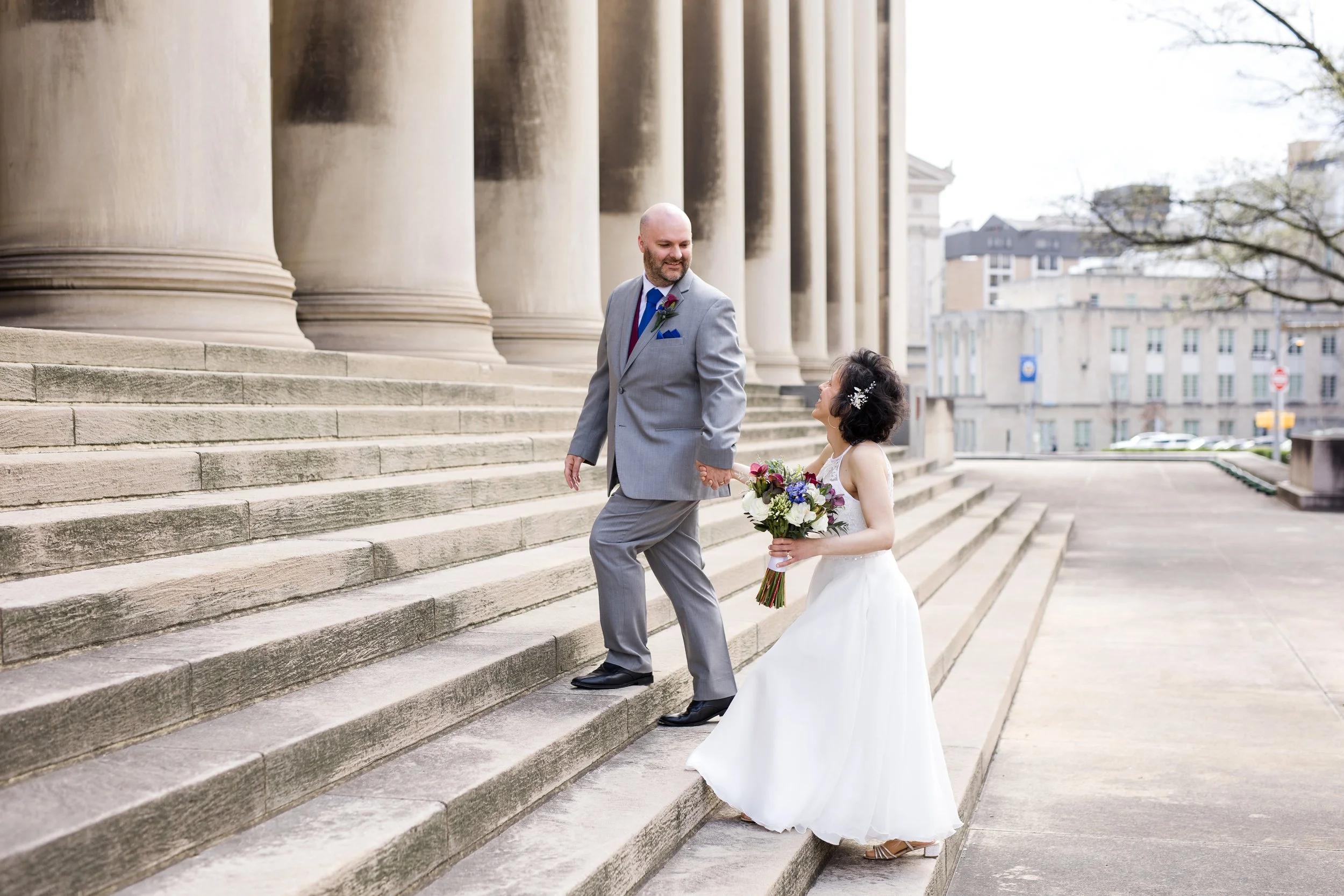 A wedding couple walk up the steps of the Mellon Institute after saying their vows. They stare at each other. The bride holds a lovely bouquet.