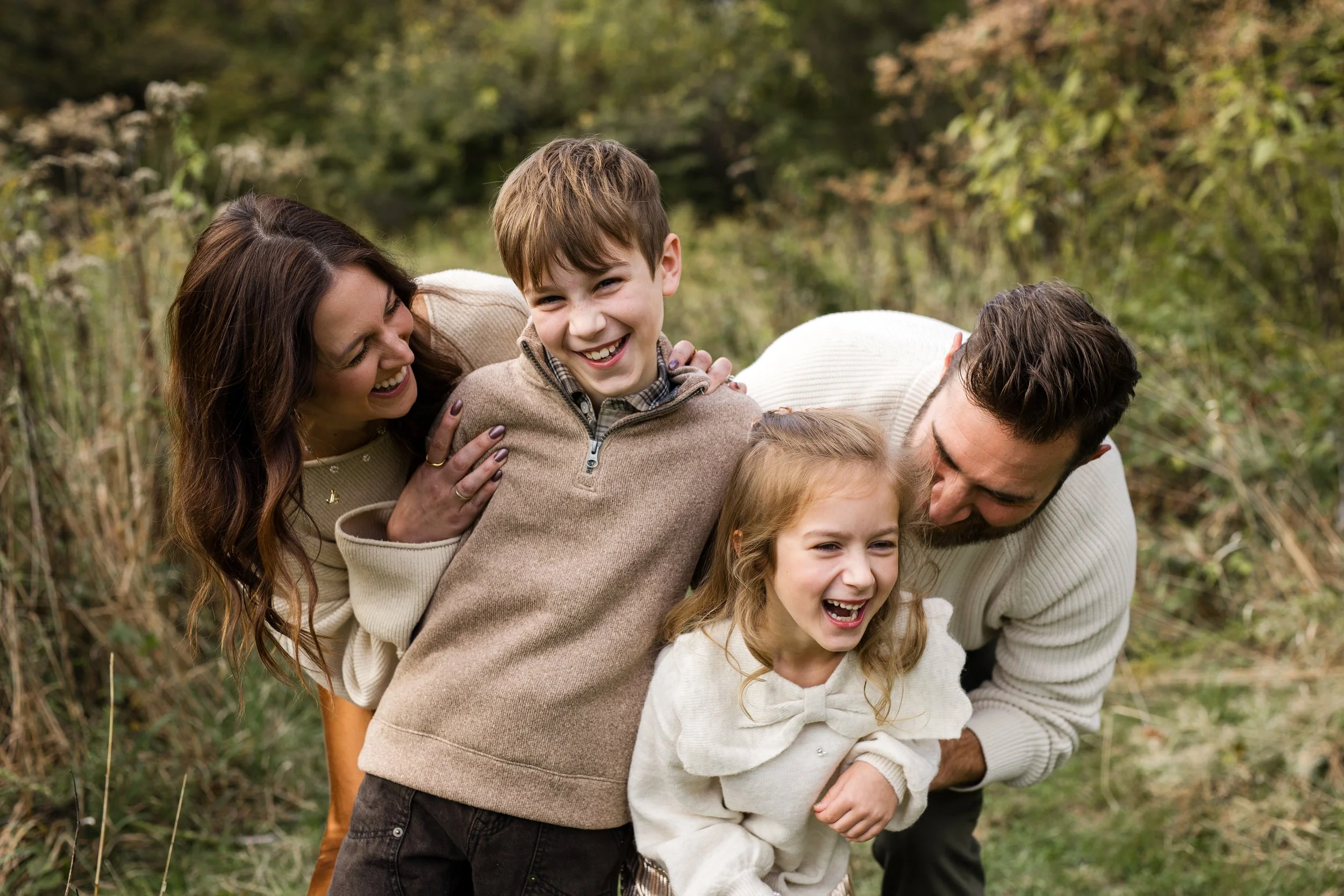 Parents tickle and hug their kids, all dressed in creme and smiling