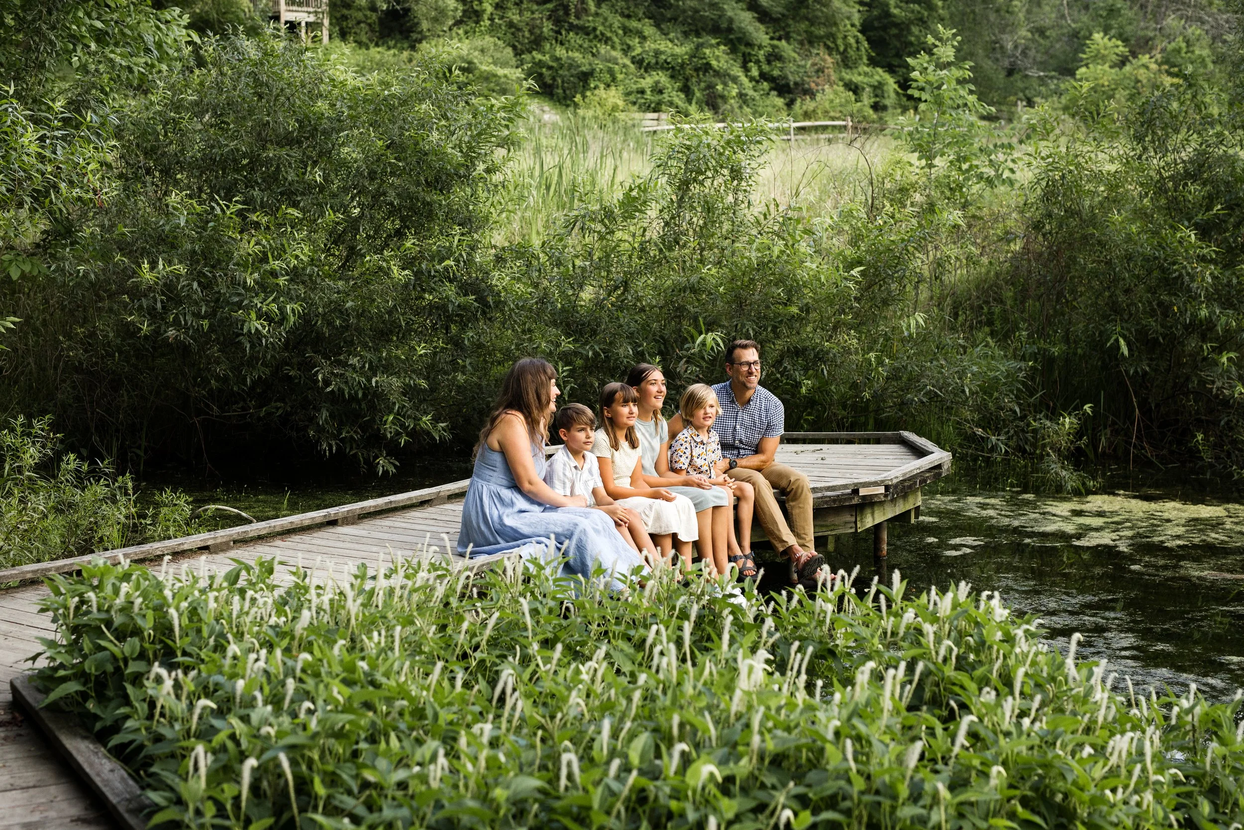 Parents and their 4 kids sit on the edge of a picturesque dock at Beechwood Nature Reserve.