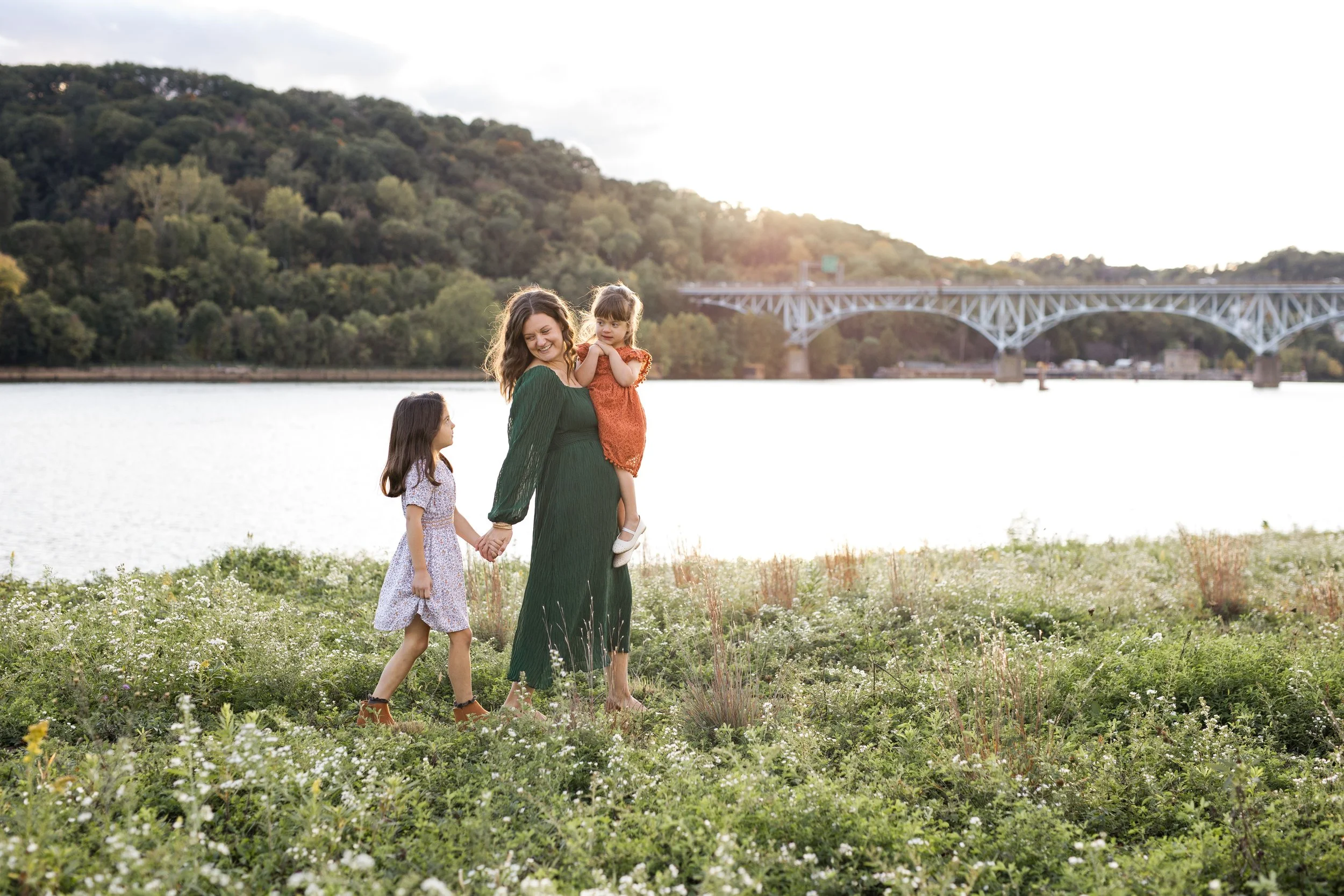 A family walks next to the Pittsburgh river and bridges in tall grasses and plants