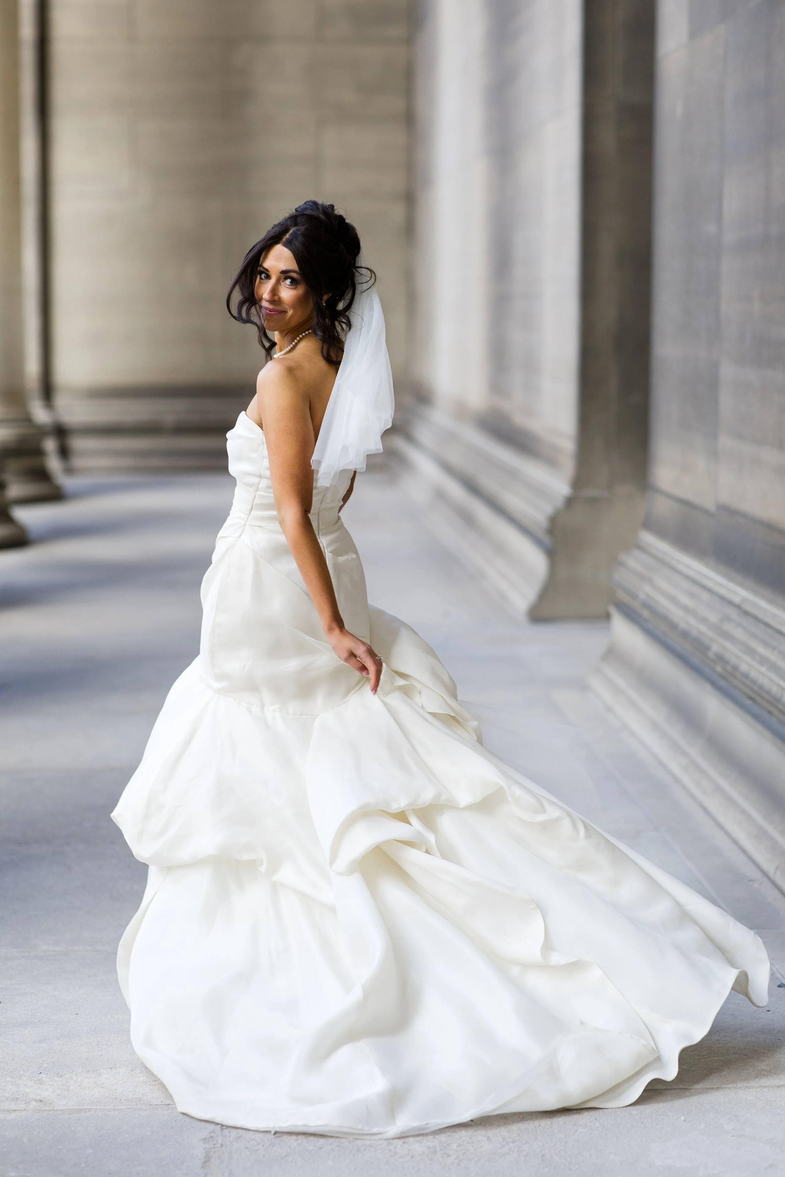 A bride turns to smile at the photographer, as she runs down a stone hallway