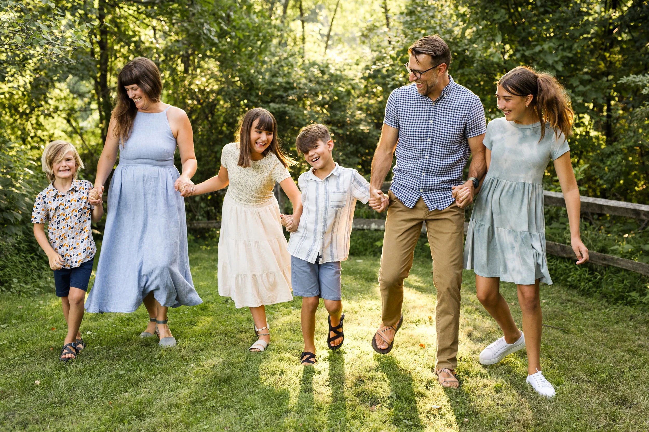 A family of 6 walks and laughs together in beautiful sunlight with a wooden fence behind them.