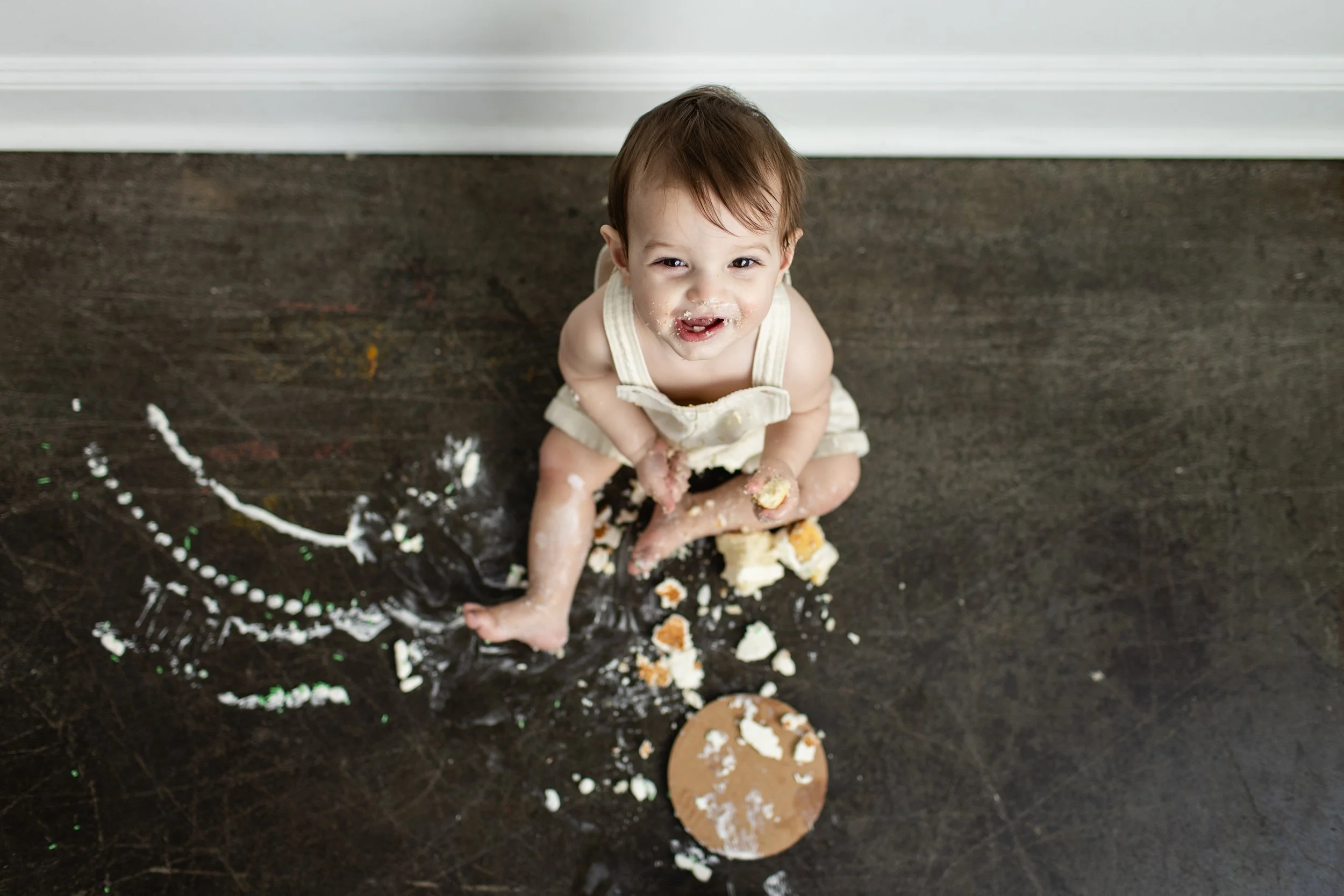 One year old smiles up at the camera while he sits in a pile of smashed cake in a Pittsburgh studio.