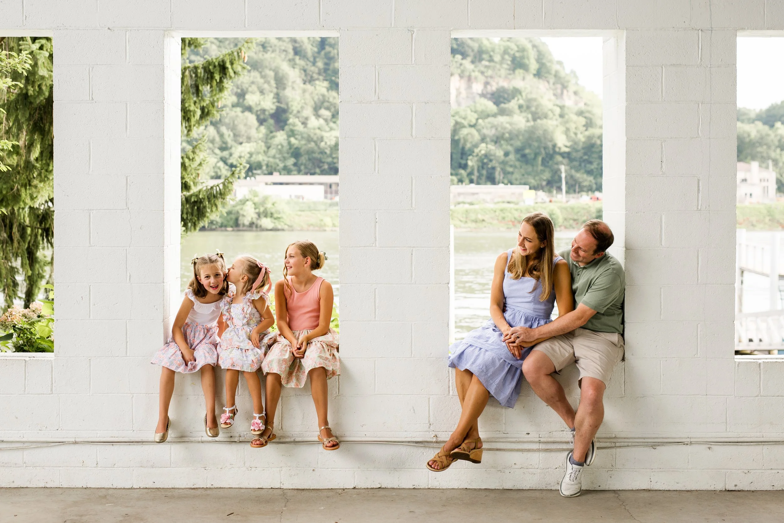 A family sits in the windowsills of the building at Aspinwall Rivertrail Park. The sisters whisper to one another