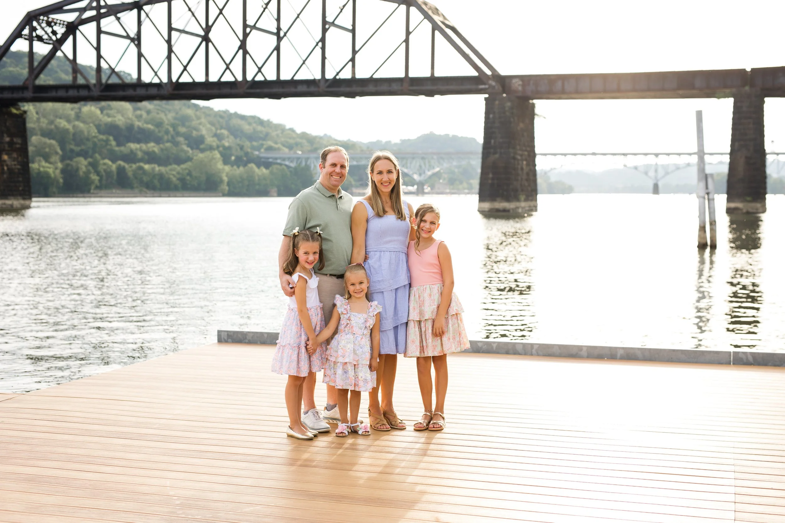 A family stands on a dock in front of one of Pittsburgh's iconic rivers. Everyone smiles