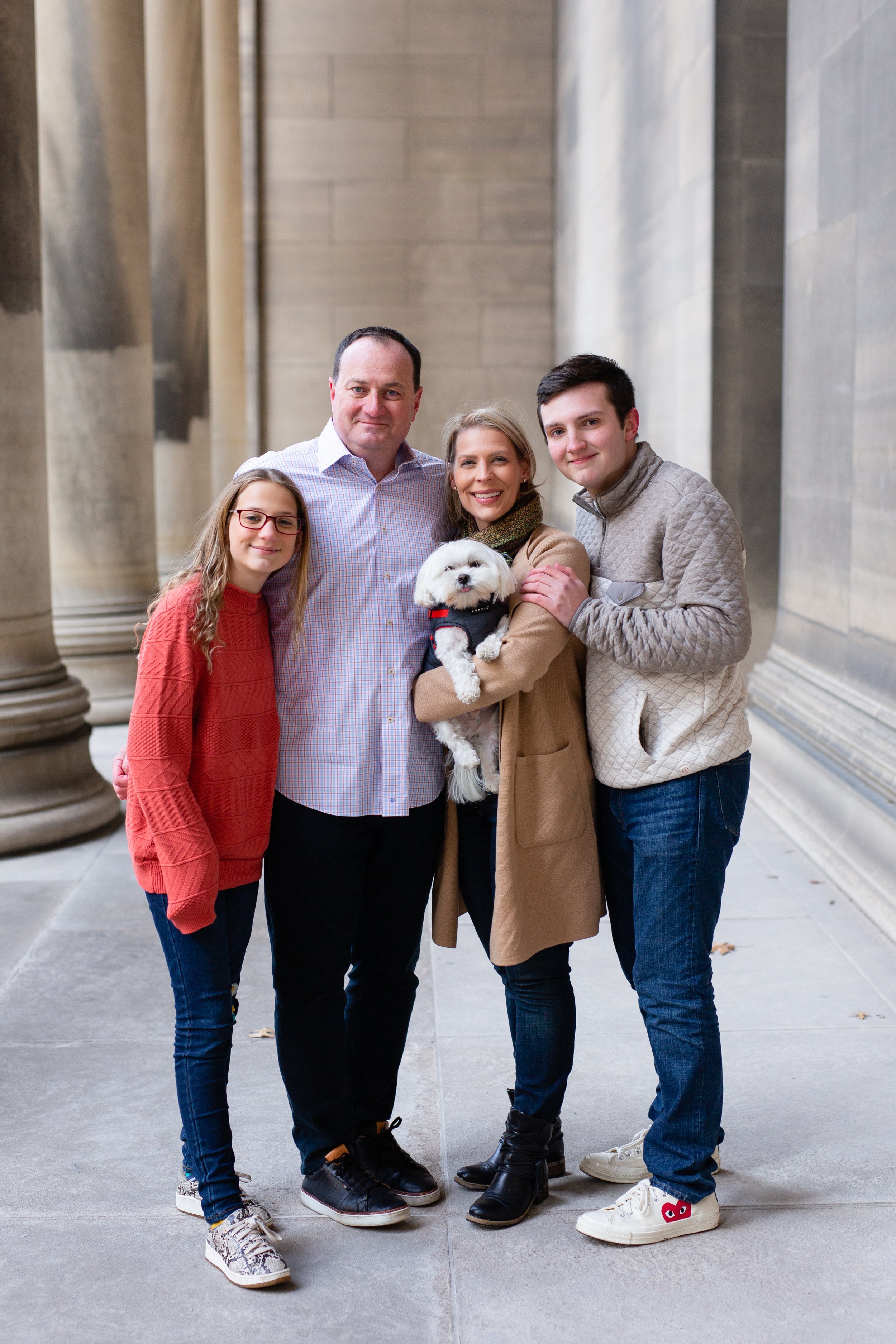 A family snuggle closely with their small dog as they stand under the cover of the Mellon Institute awning.