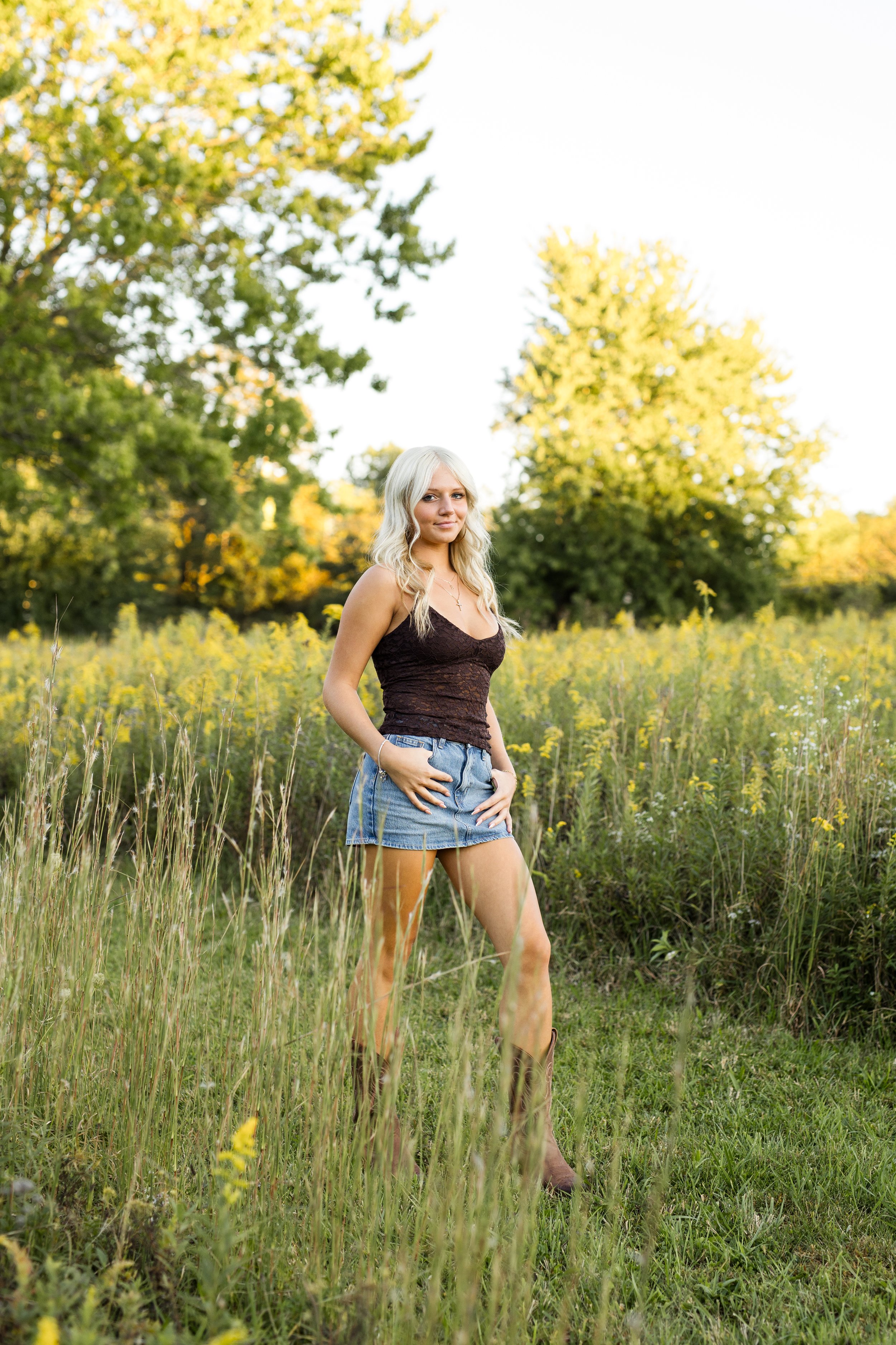 Girl in jean skirts and a tank stands in a field of yellow flowers