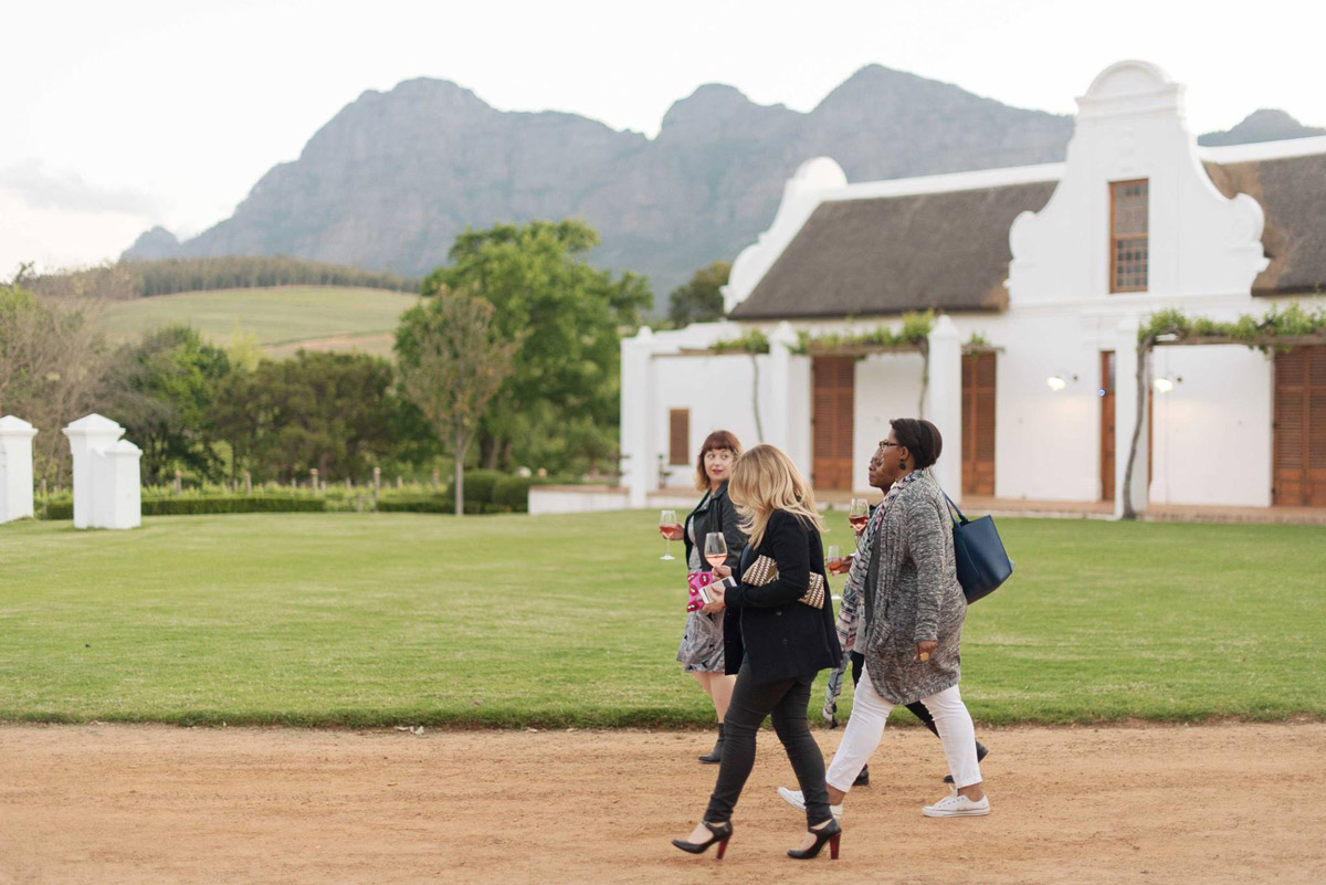 Four well-dressed women walk through a vineyard, wine glass in hand, during a SecretEATS afternoon event.