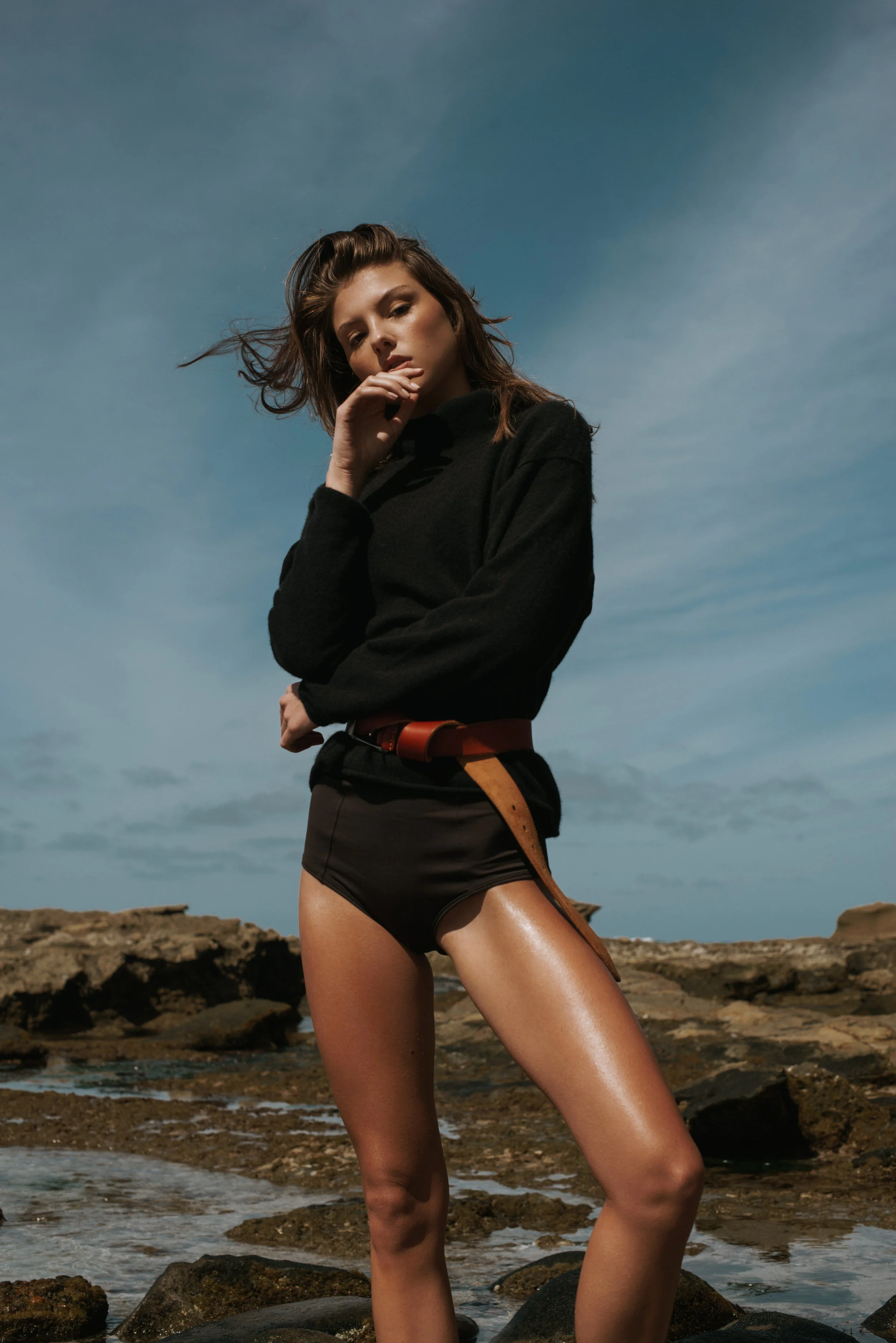  Fashion-forward swimwear shoot with textured sweater and wind-blown hair on rocky coastline 