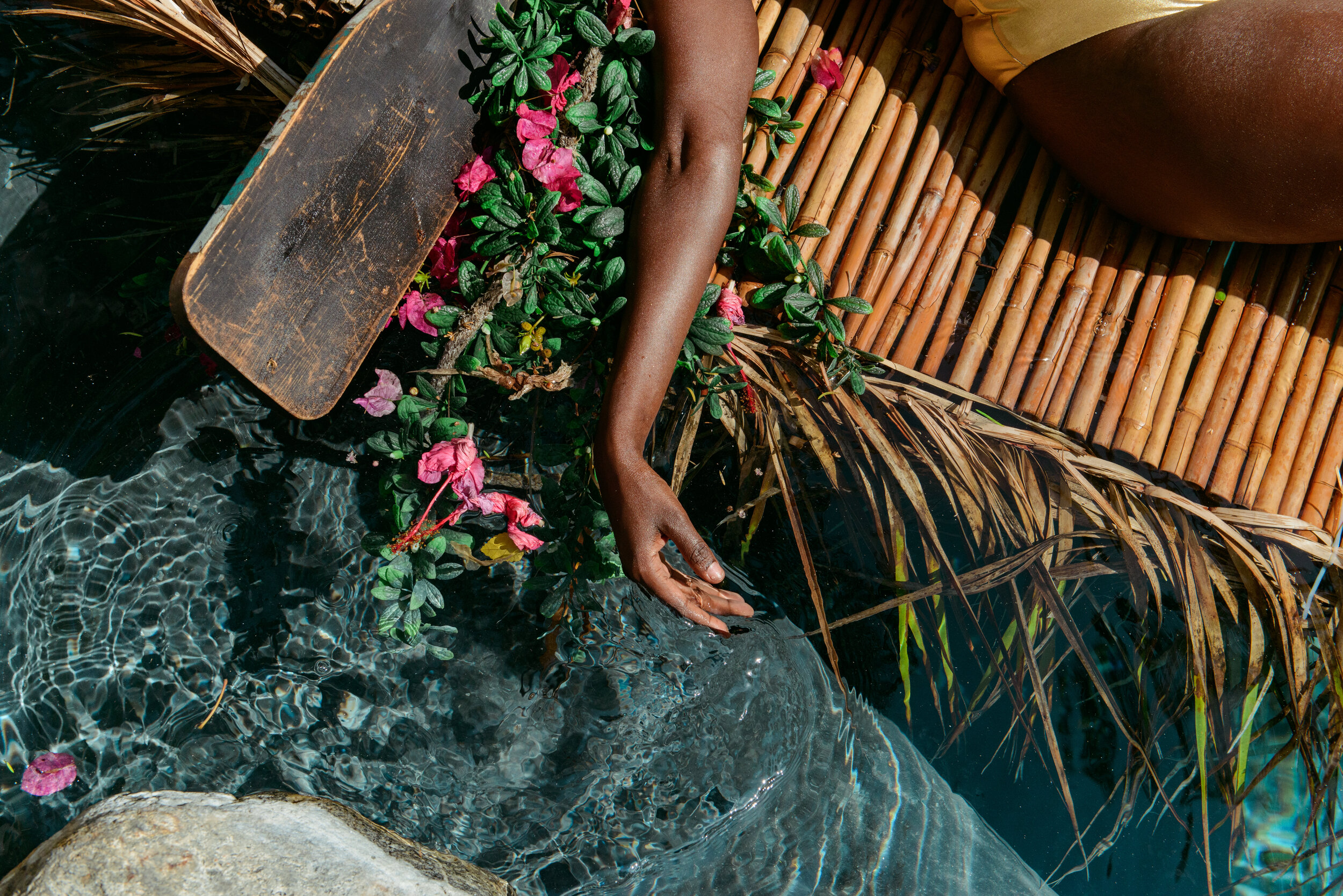  Detail shot of a model's arm in tropical swimwear scene with flowers and still water, photographed by Kristina Yamamoto 