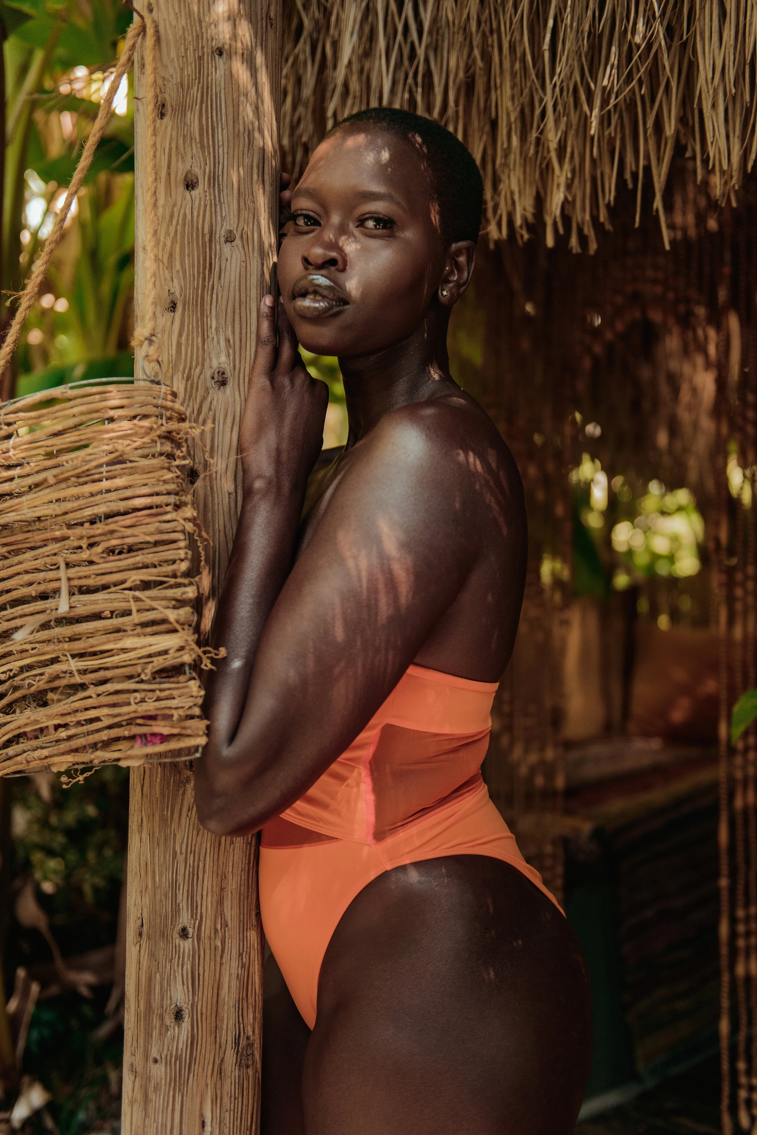  Bold editorial swimwear portrait of model in orange swimsuit near tropical Bali hut 