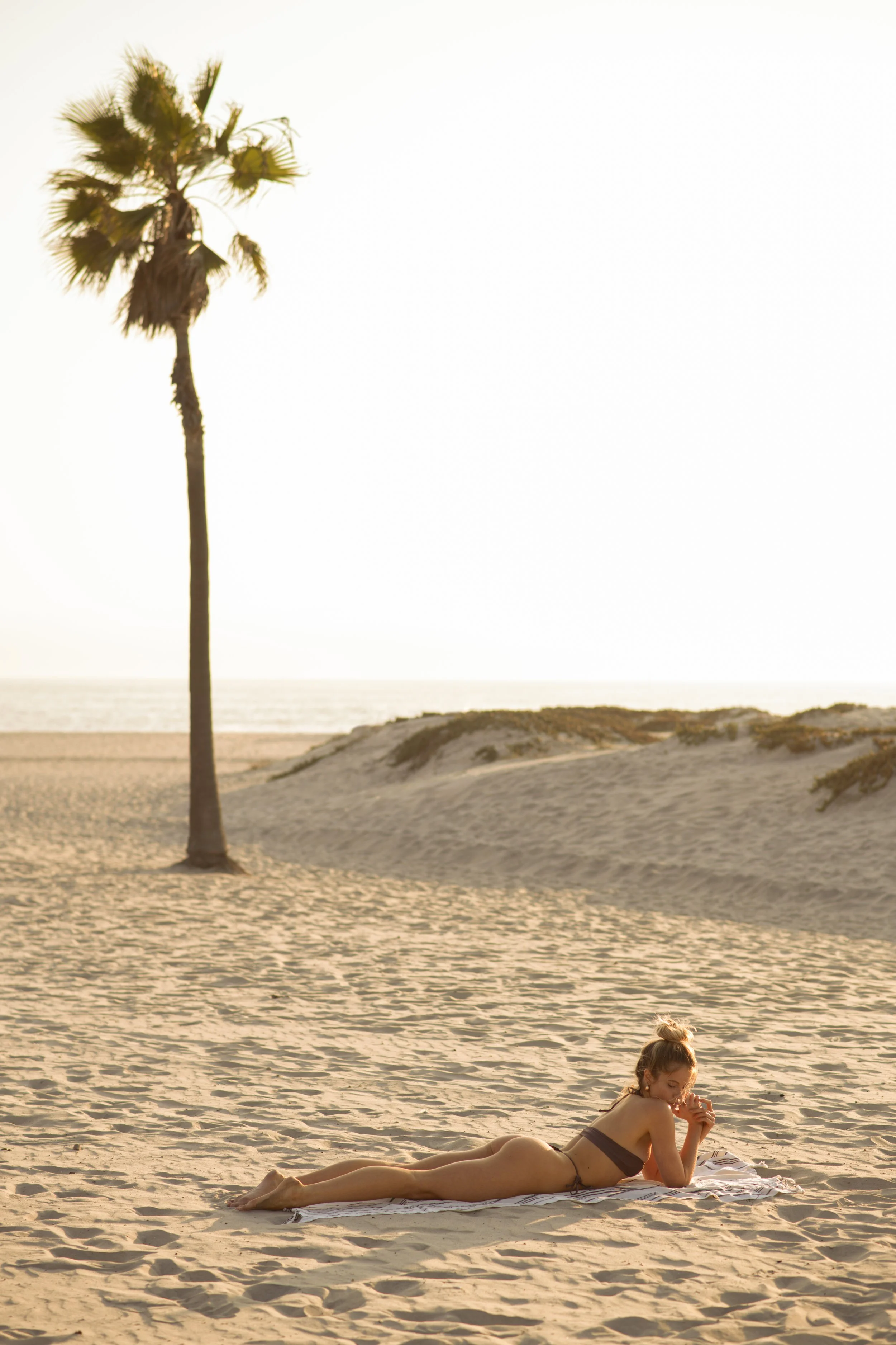  Swimwear editorial of model lying on open beach at golden hour, captured with natural light and soft shadows 