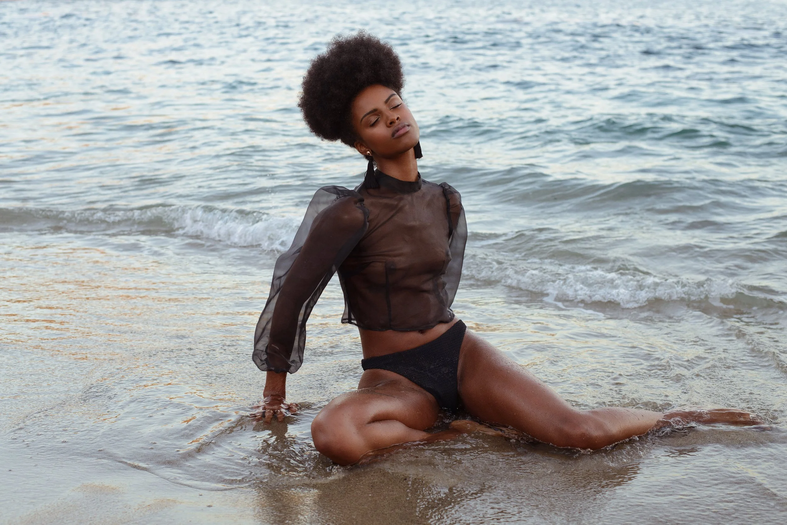  Fashion-forward swimwear shot with model in sheer black top and bikini, posing in the surf 