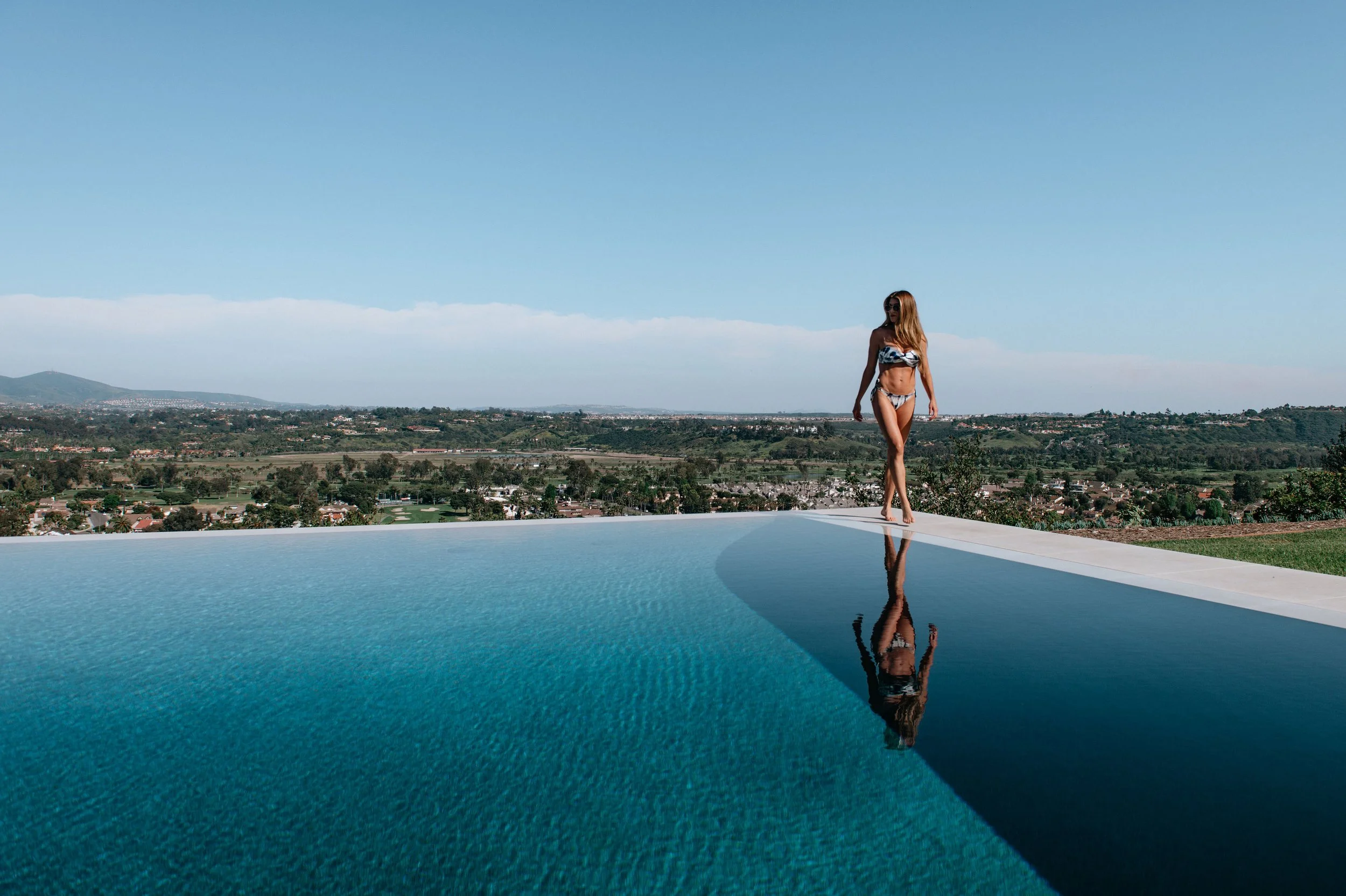  Editorial swimwear campaign with model walking along infinity pool edge overlooking landscape 