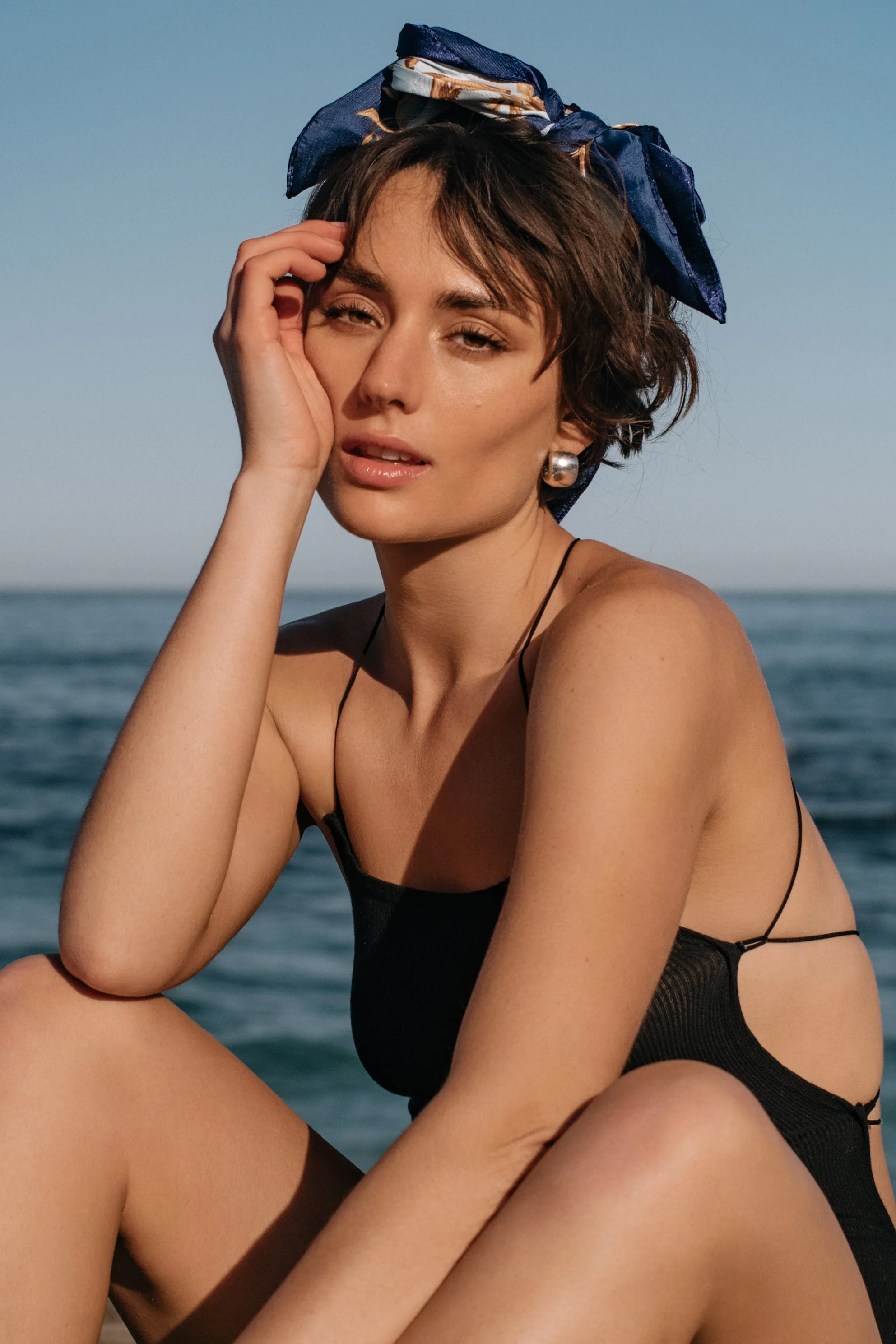  Sunlit swimwear portrait of model in black cutout swimsuit and headscarf, photographed on the California coast 