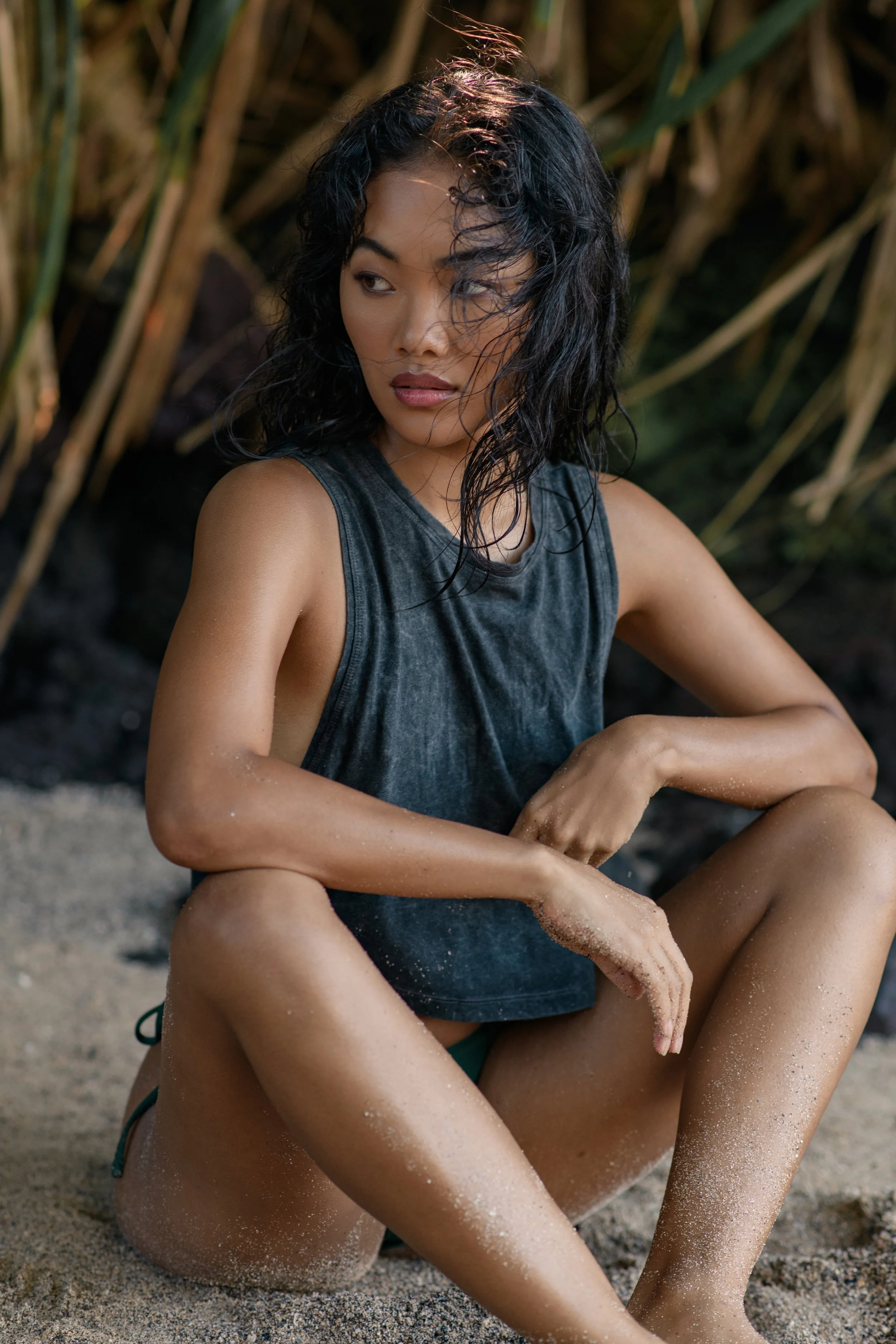  Moody swimwear portrait with model seated on sandy beach in wet charcoal tank and minimal styling 