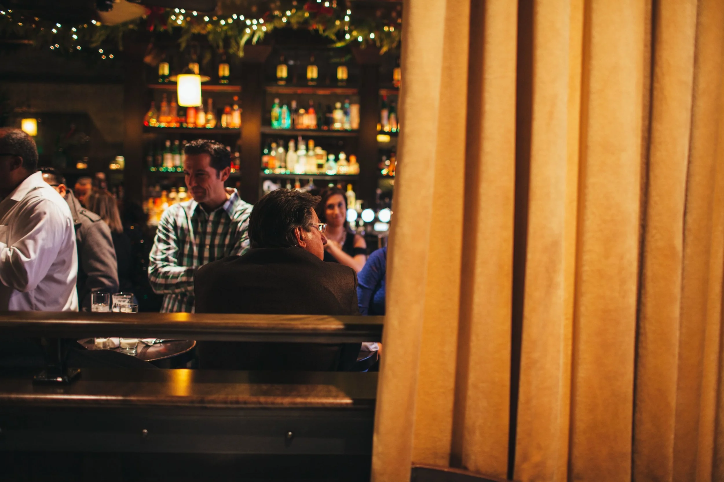 Artistic shot through the curtains, peeking into The Gage's bar area, where guests enjoy each other's company.jpg