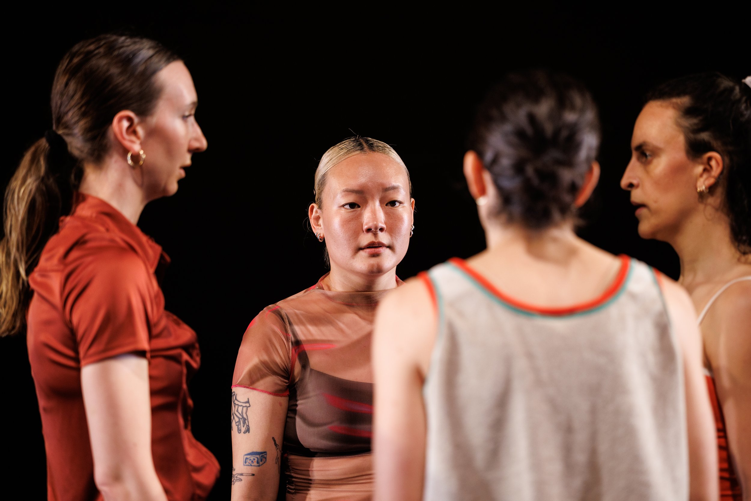 Four women standing in a circle talking, with a black background.
