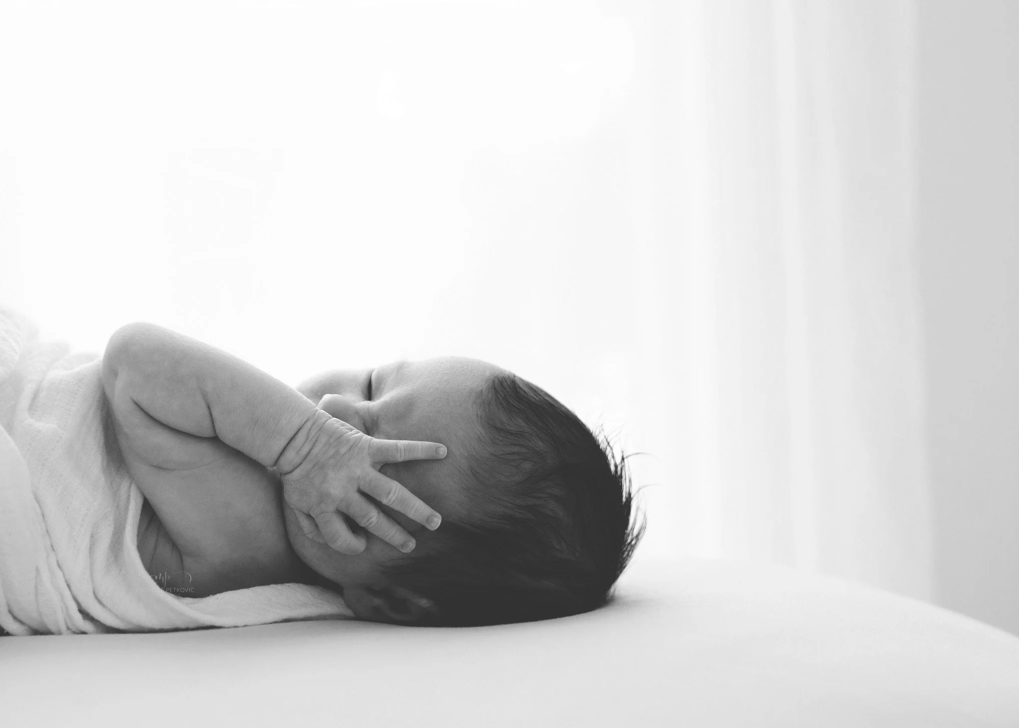 A black and white photo of an 8 day old baby laying on a bed by a window at their newborn photography session in Adelaide