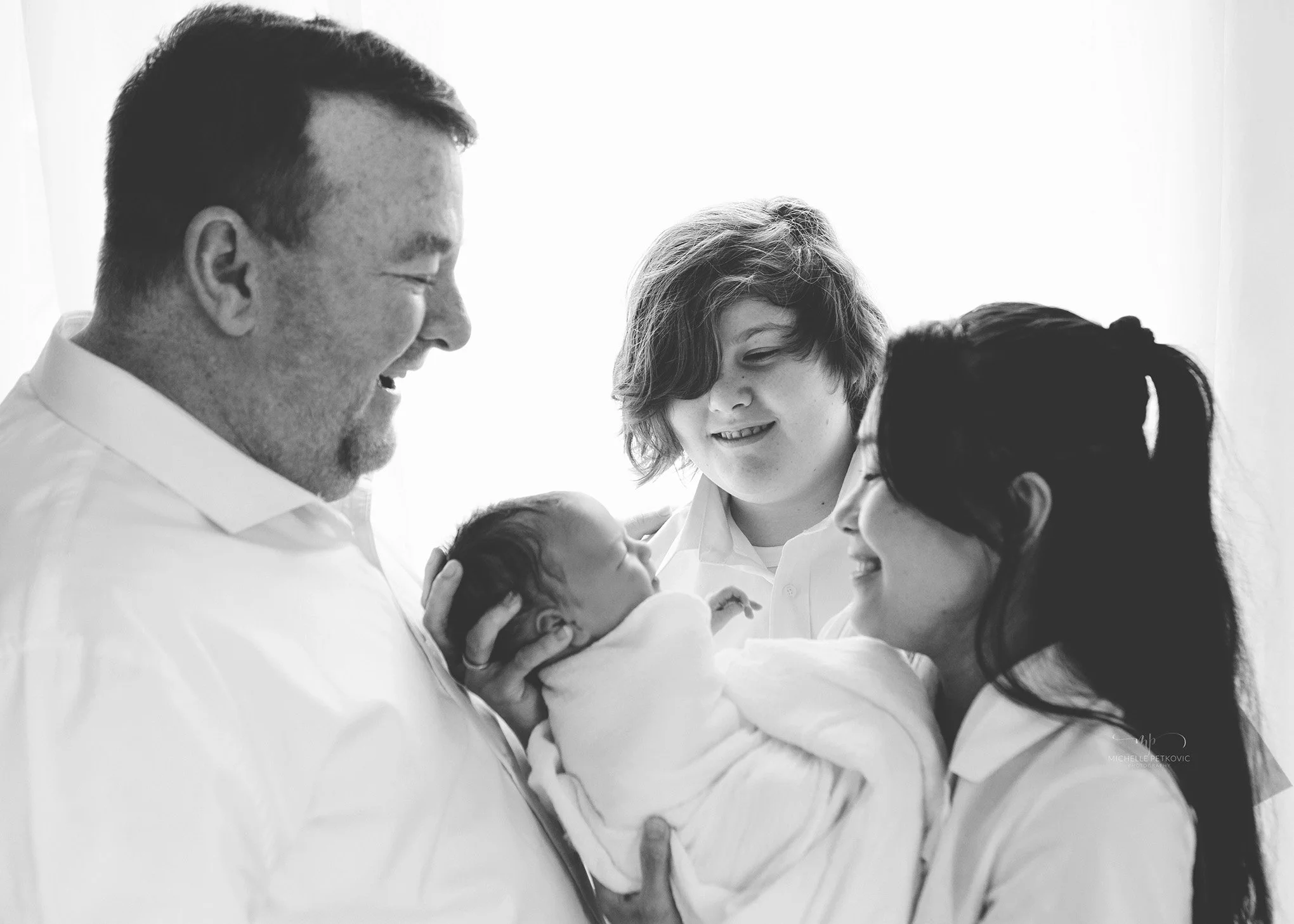 family holding a newborn baby with big brother looking on at their newborn photography session in Adelaide
