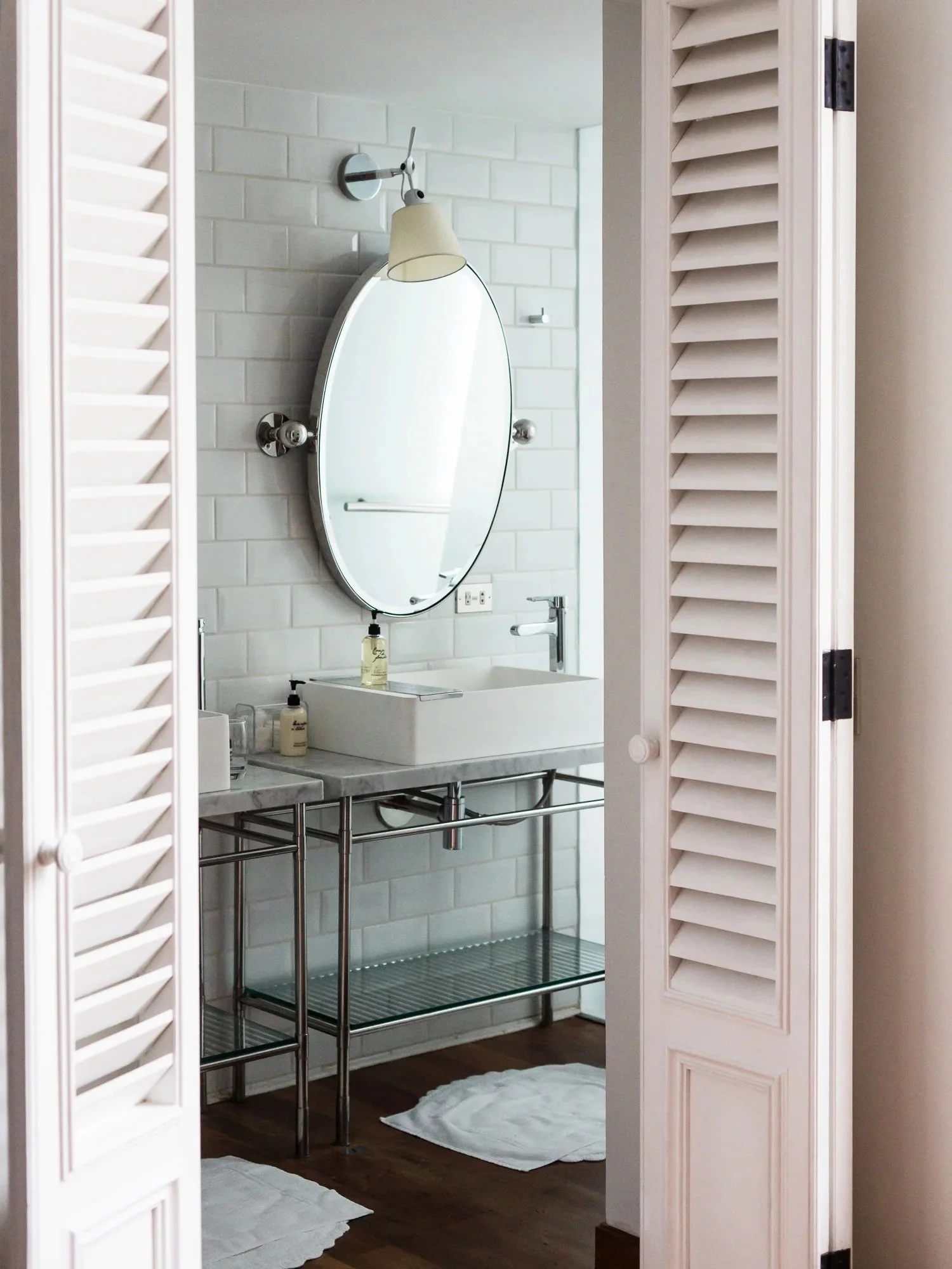 eclectic bathroom styling in north london house. Feestanding wash bsain with a tradtional stle, oval mirror and Louvre doors for a french flair. metri tyles floor to ceiling.