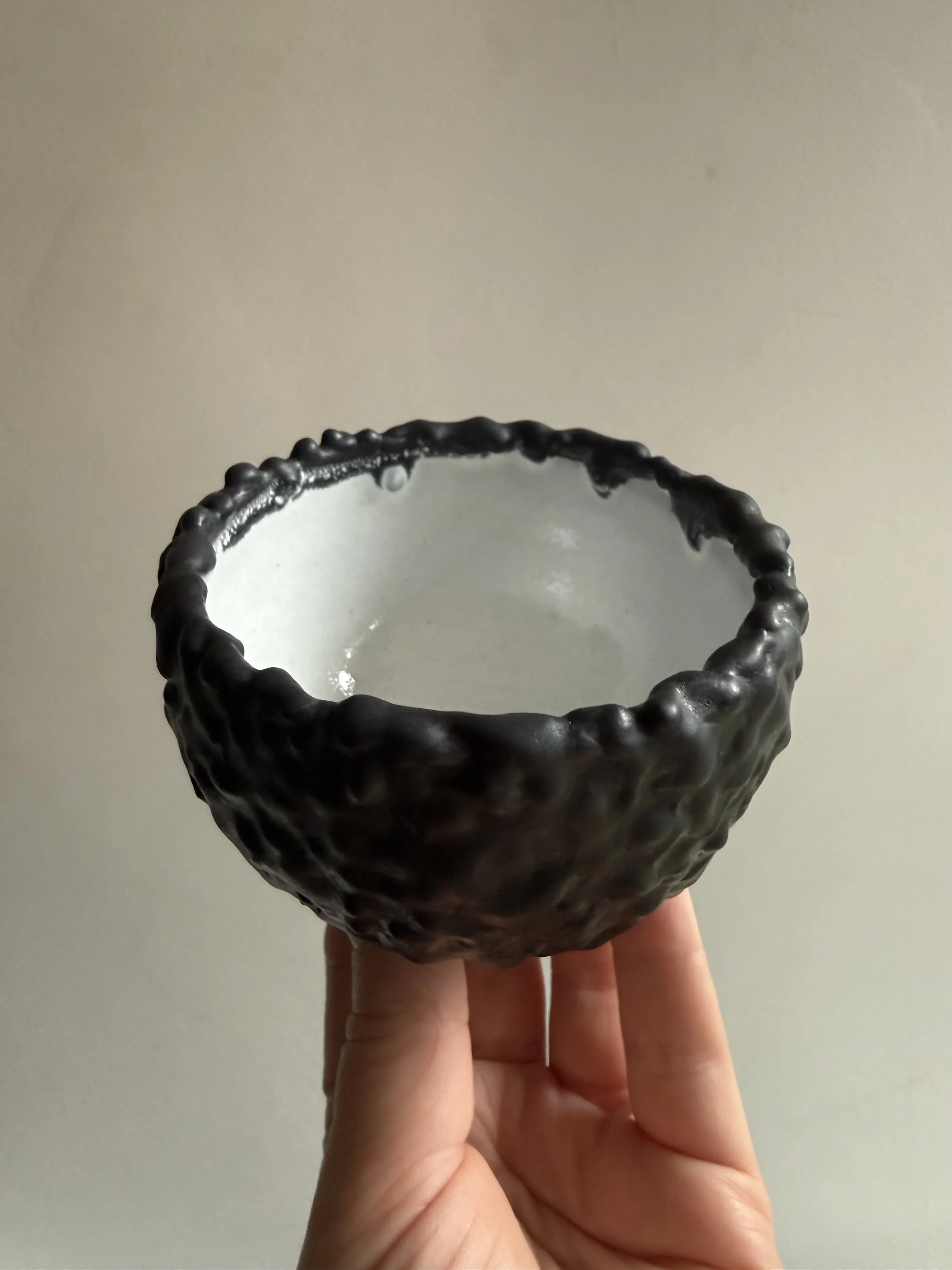 small hand -hrown pottery bowl by Caroline Couzens wtth a delightfully textured matt black exterior and glossy white interior glaze