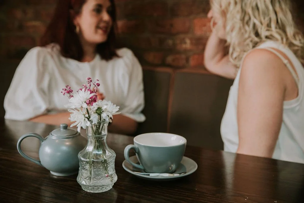 Two small business owners chat in a cafe over a pot of tea.