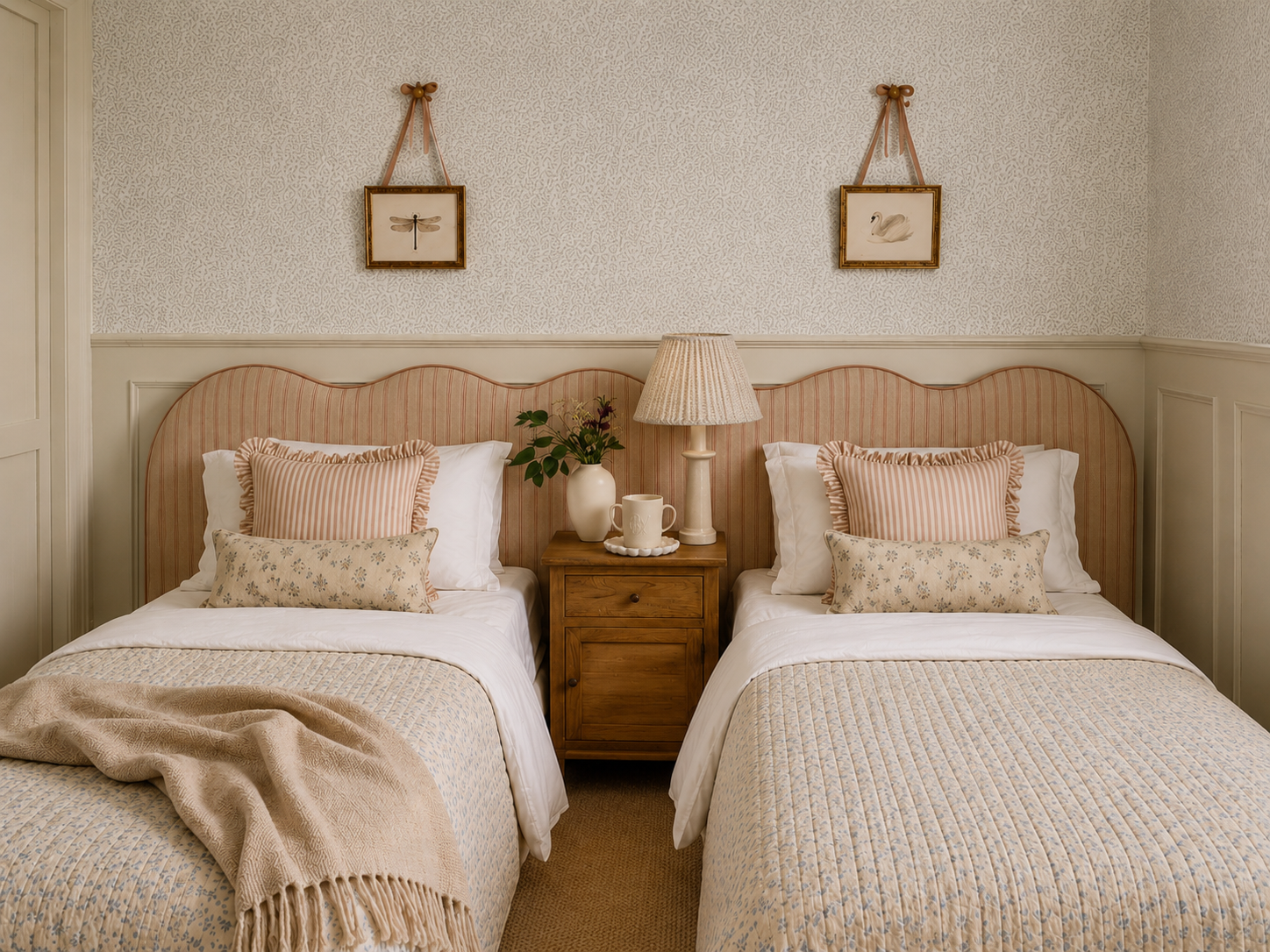 A cozy bedroom with two beds, a wooden nightstand, a table lamp, a vase with flowers, and framed artwork of a dragonfly and a swan on the wall.