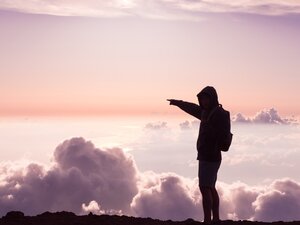 Person on a mountain at sunrise above clouds pointing into the distance, representing Open Education by Blackboard free online ecology courses.