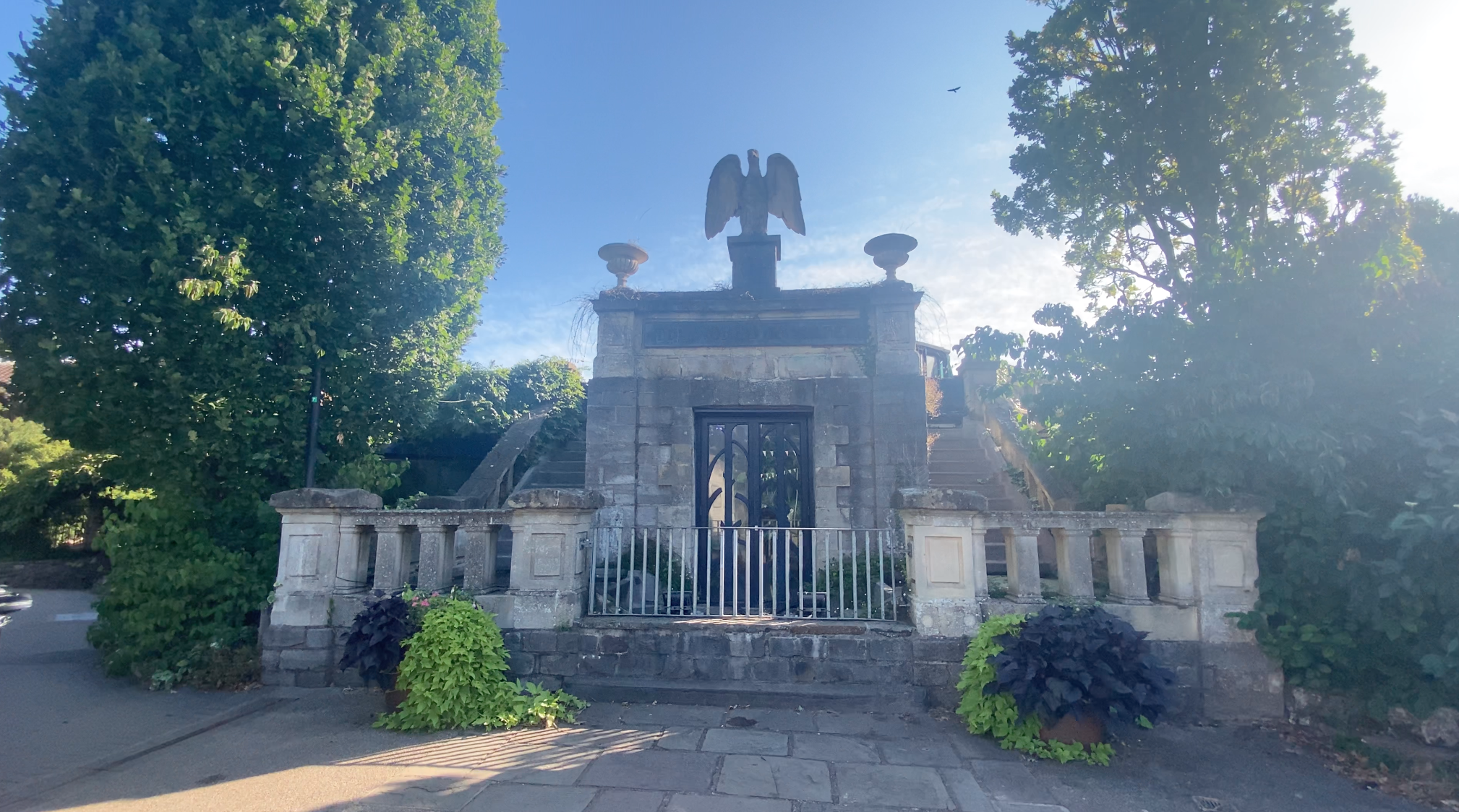 The closed entrance to Bristol Zoo Gardens in Clifton, showing a stone gateway topped by an eagle statue and surrounded by trees.