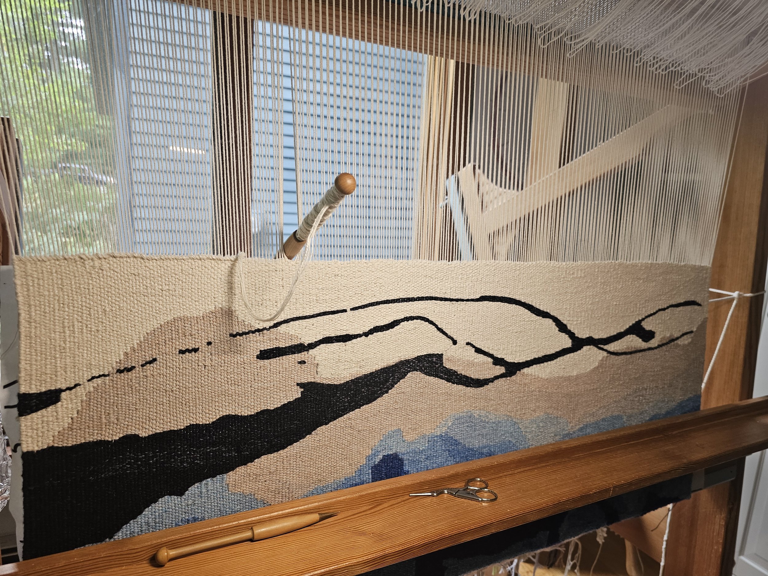 Handwoven tapestry in progress on a loom. Fiber art depicting the ocean's edge.