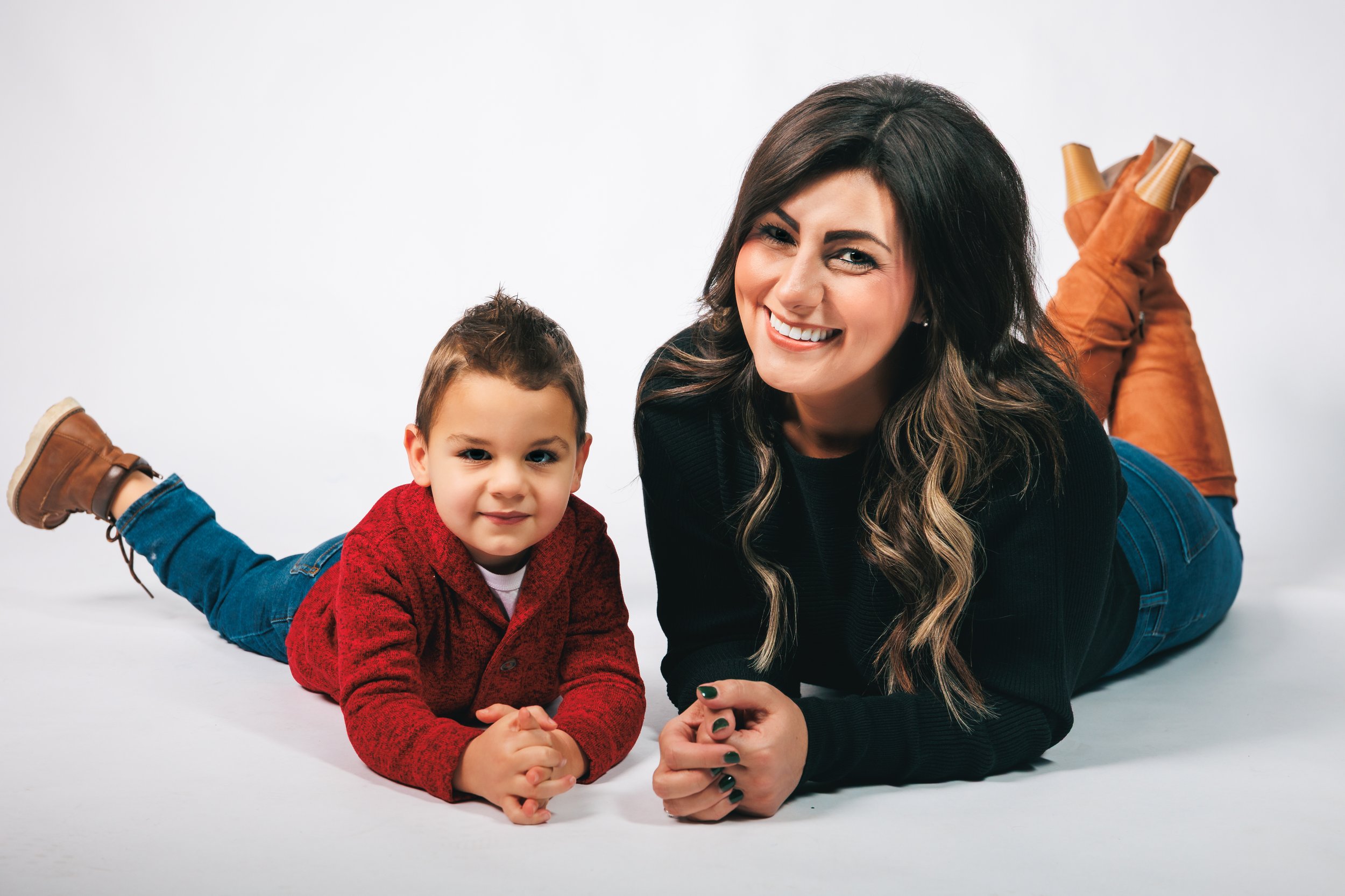 A woman and a young boy lying on their stomachs on a white background, smiling and looking at the camera.