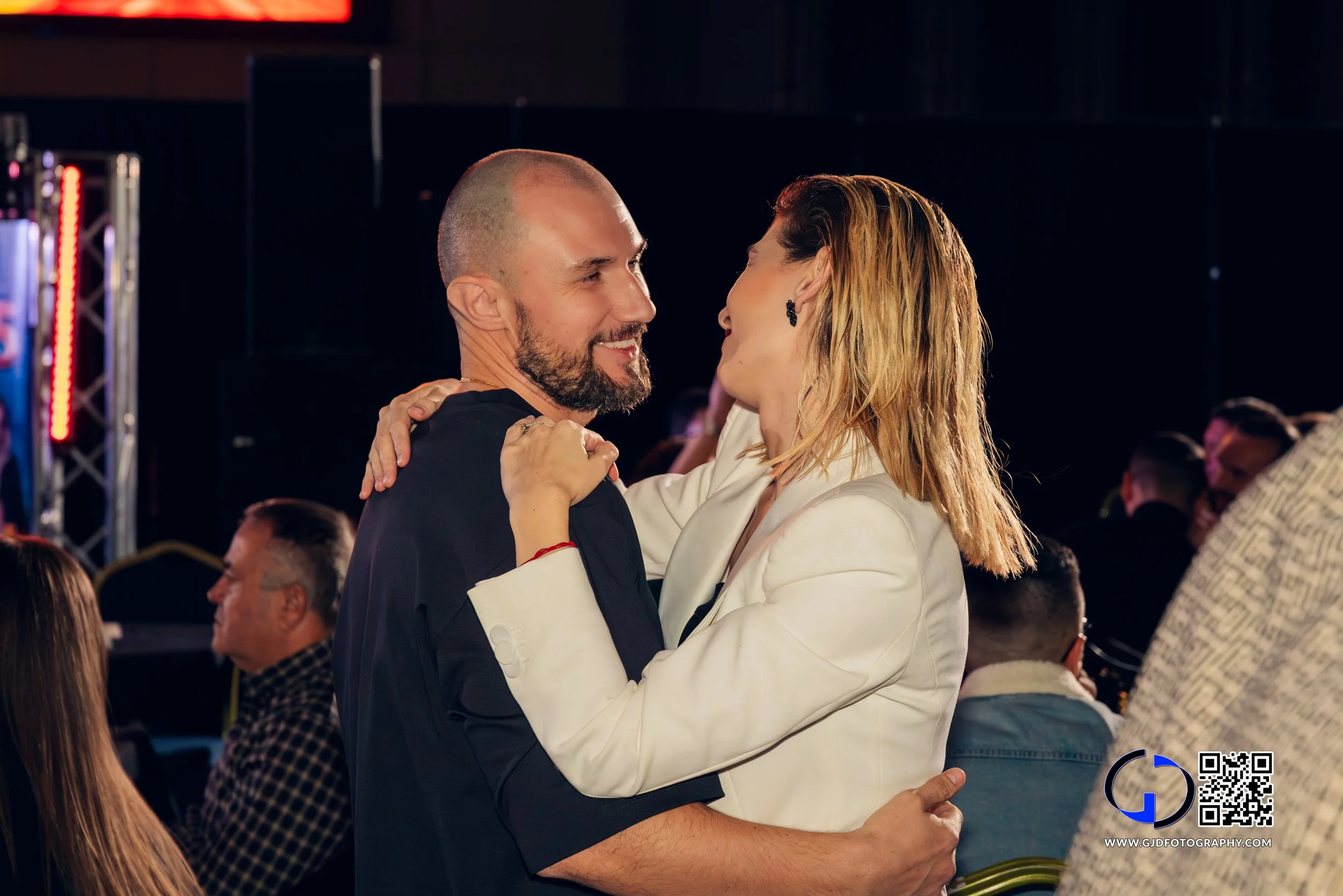 A man and woman dancing closely at a social event, smiling and looking eye to eye.