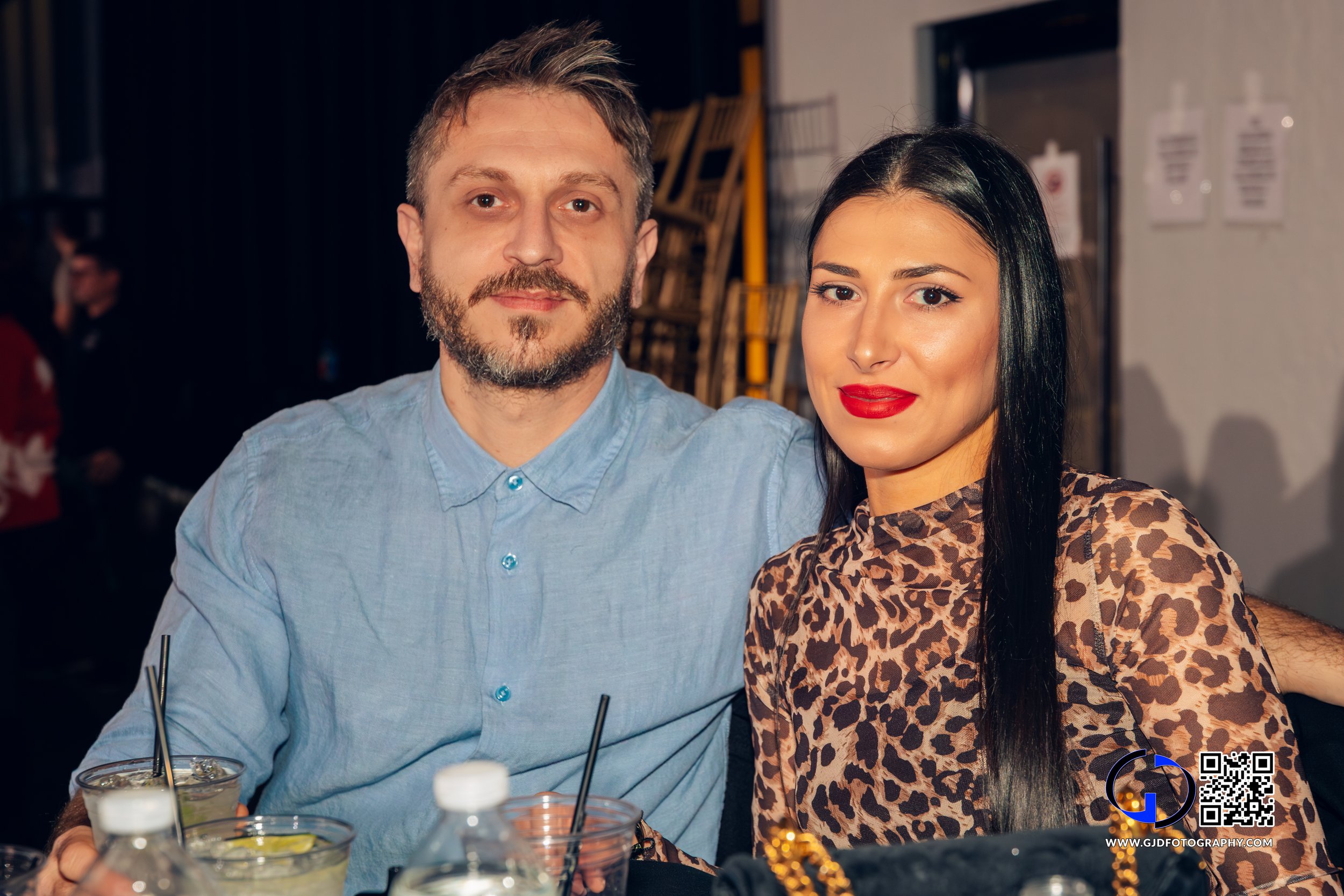 A man and woman sitting together at a social event with drinks on the table in front of them.