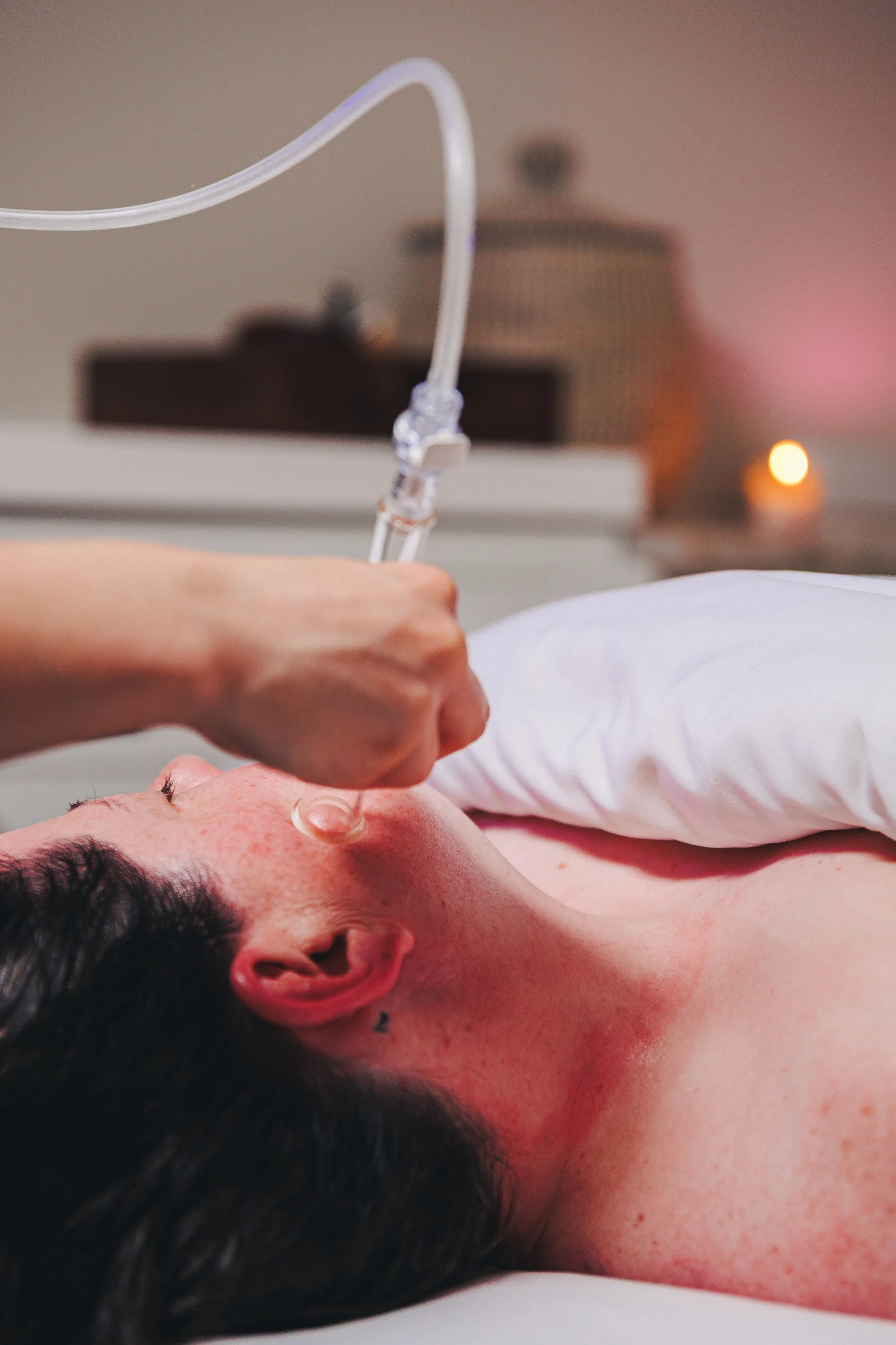 Person receiving facial treatment with a facial mask or serum applied to their face, in a relaxed setting with soft lighting.