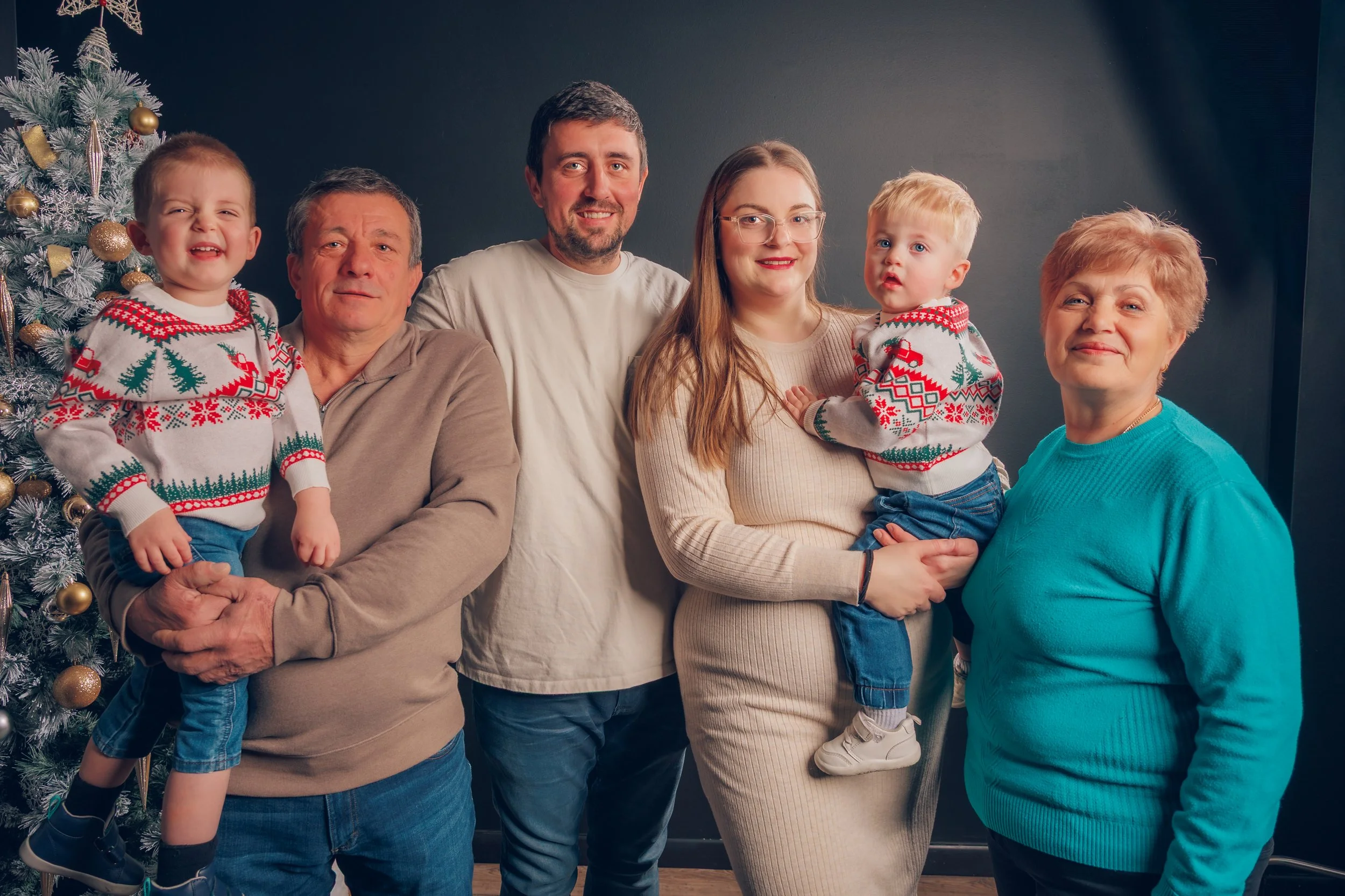 A family of six celebrating Christmas, posing in front of a decorated Christmas tree, all wearing holiday sweaters and smiling.