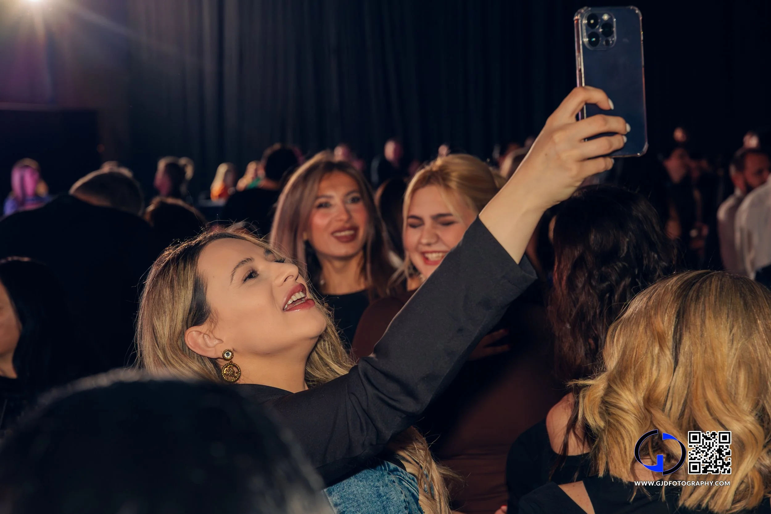 Woman taking a selfie at a crowded event with others smiling and posing.