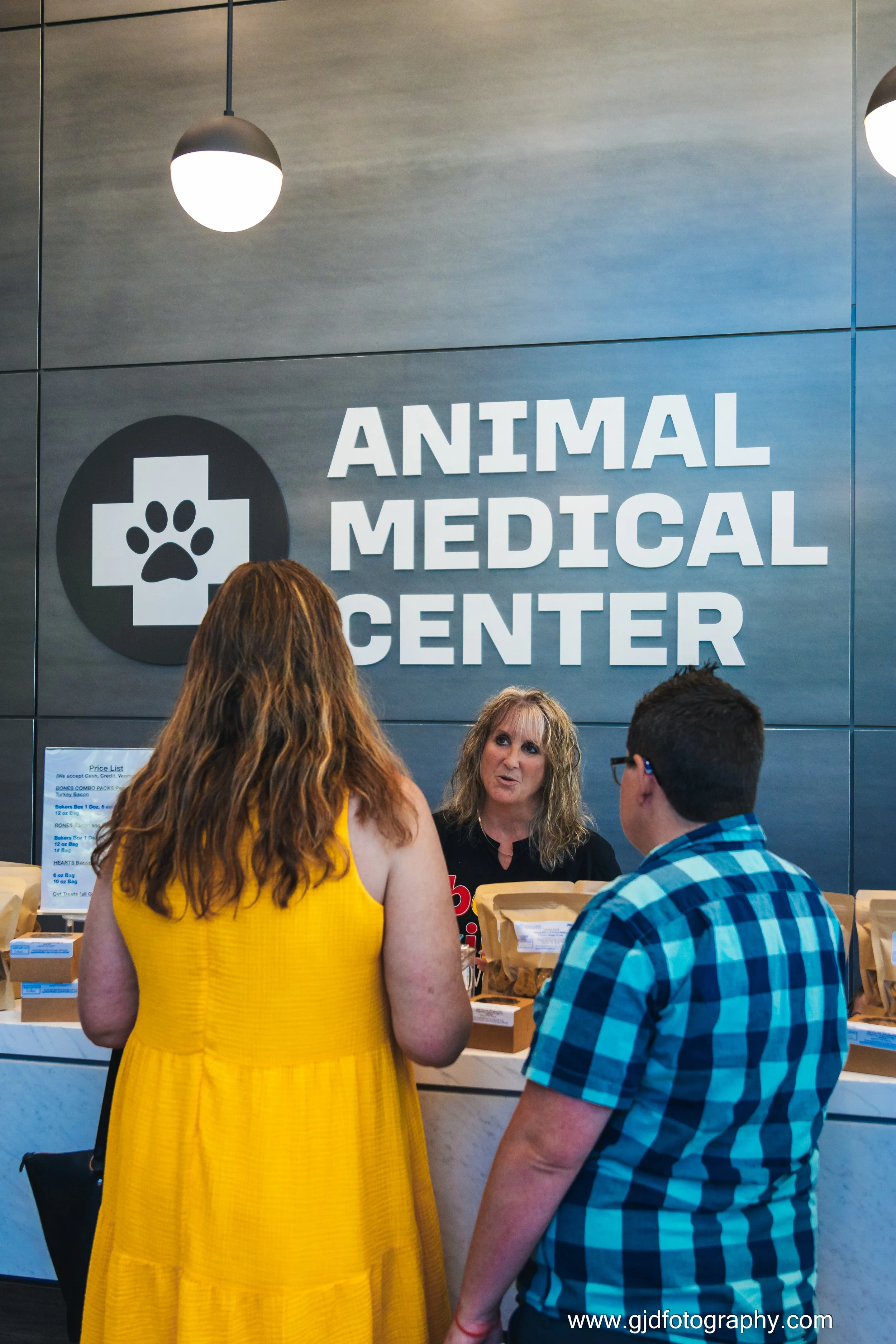 People at the counter of an animal medical center, having a conversation with a staff member, with the sign 'Animal Medical Center' visible in the background.
